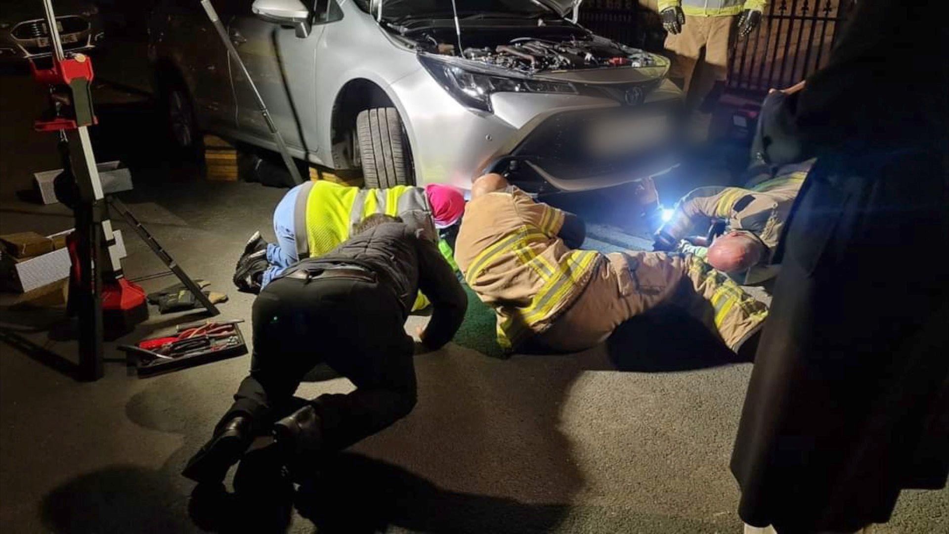 Firefighters searching under the car for the trapped kitten