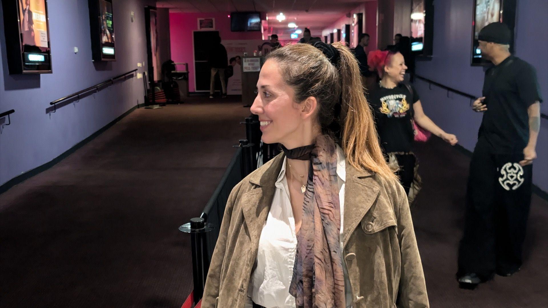 Filmmaker Georgia Zeta Gkoka stands in front of the screenings area at a cinema with her face at a right angle to the camera while smiling