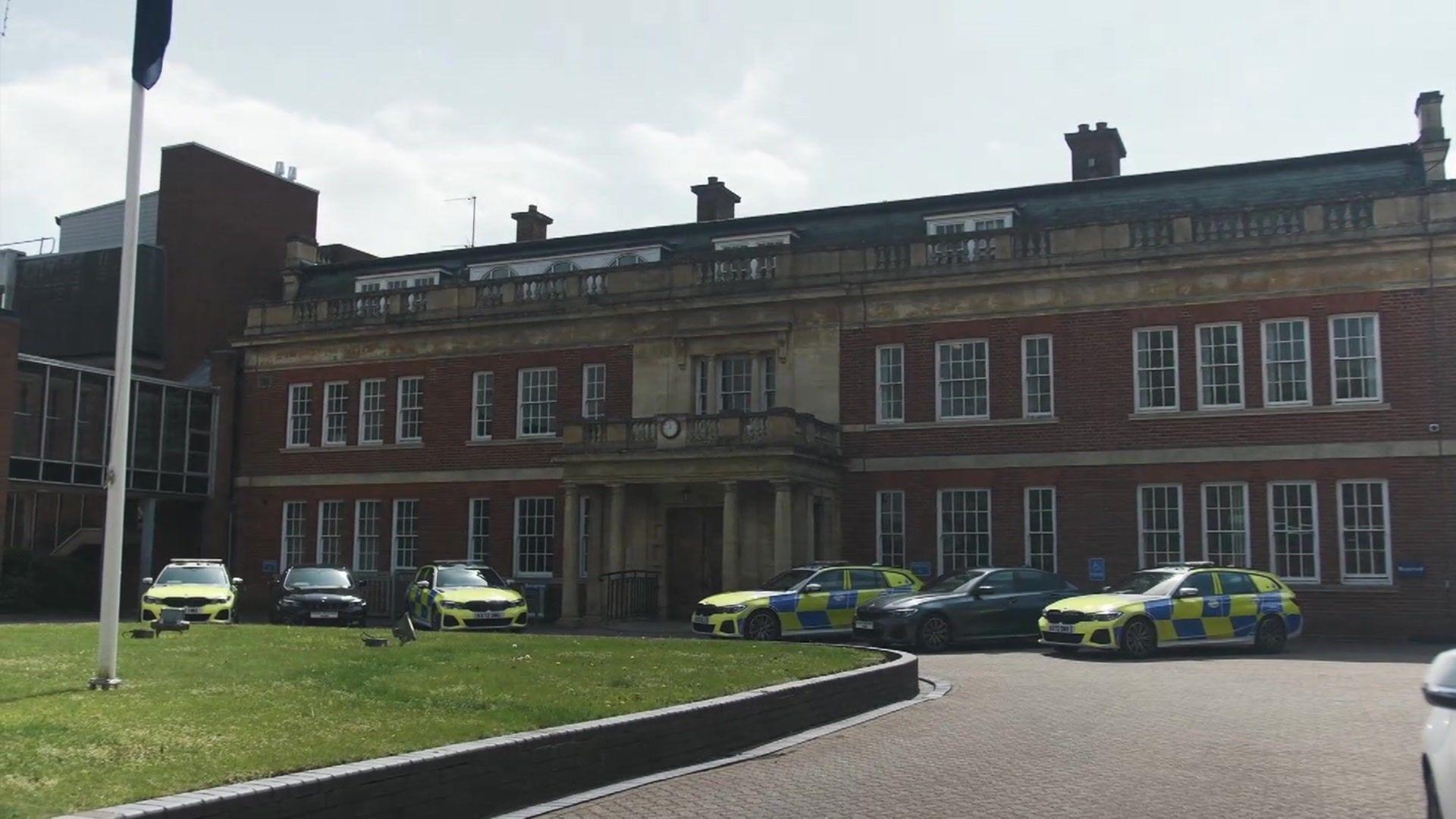 A three-storey brick building with rows of windows and six police cars parked outside.