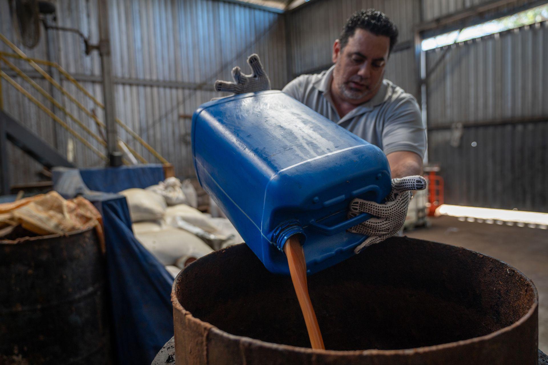 Edgardo David Guzmán pours grease from a jerry can into a drum in a warehouse in Comayagua. He is wearing protective gloves.