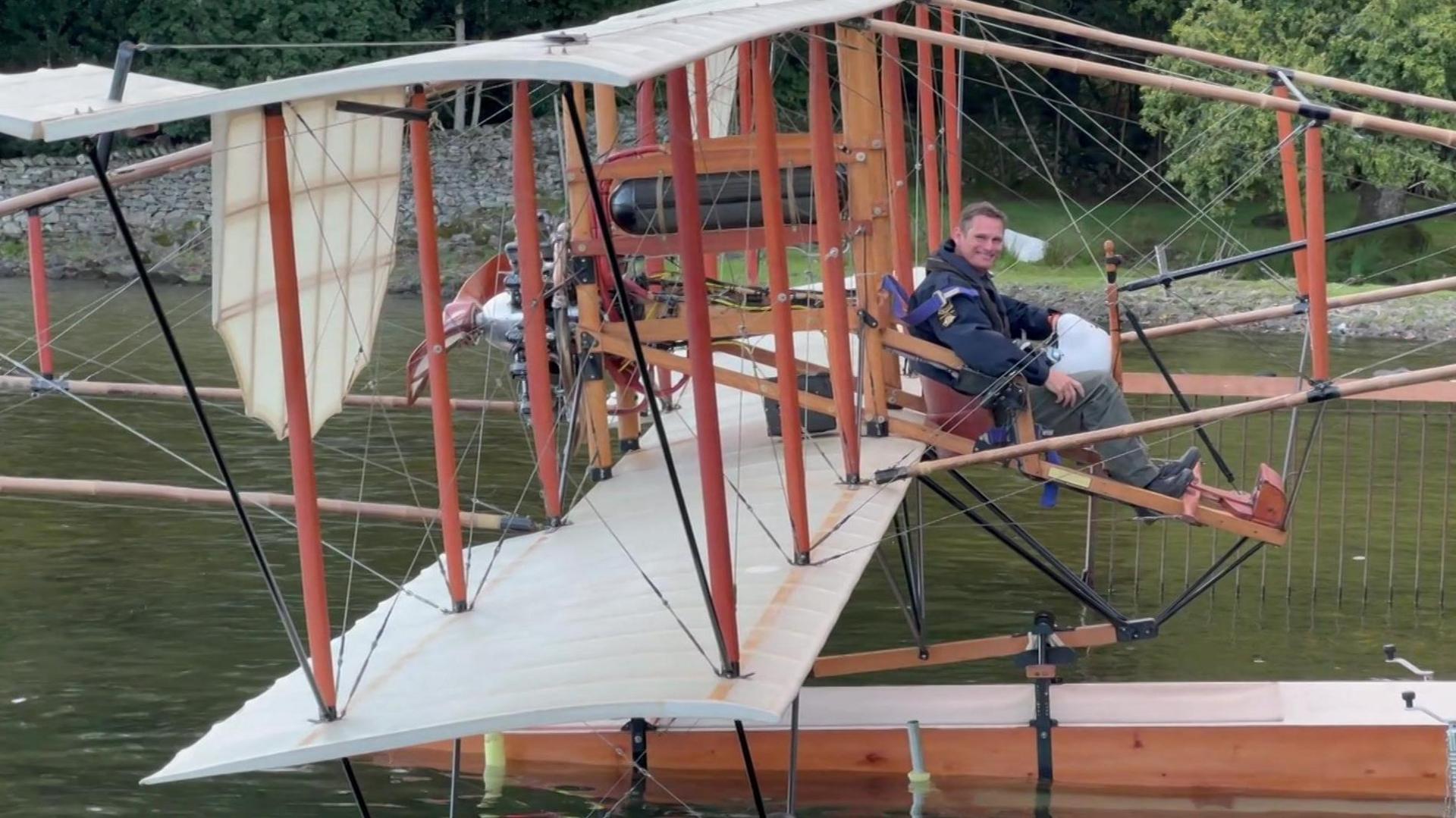 A general view of Waterbird on the water. The aircraft is pictured side on and Lieutenant Commander Götke is at the cockpit, looking at the camera and smiling.