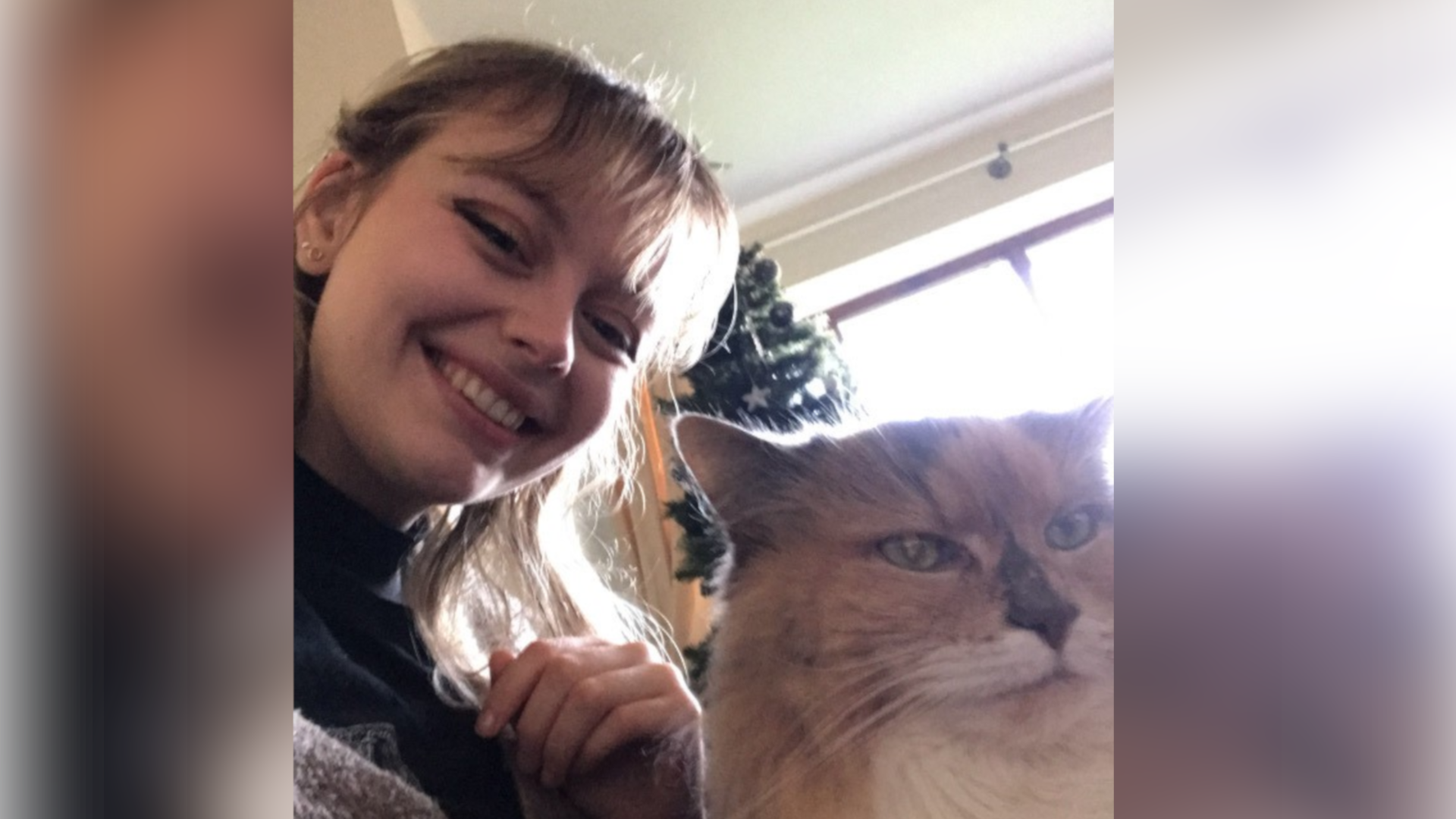 Kat Nellist in a selfie with a light brown cat. The catl has a white neck and green eyes and is looking to the right of the camera. Kat is smiling as she takes the photo