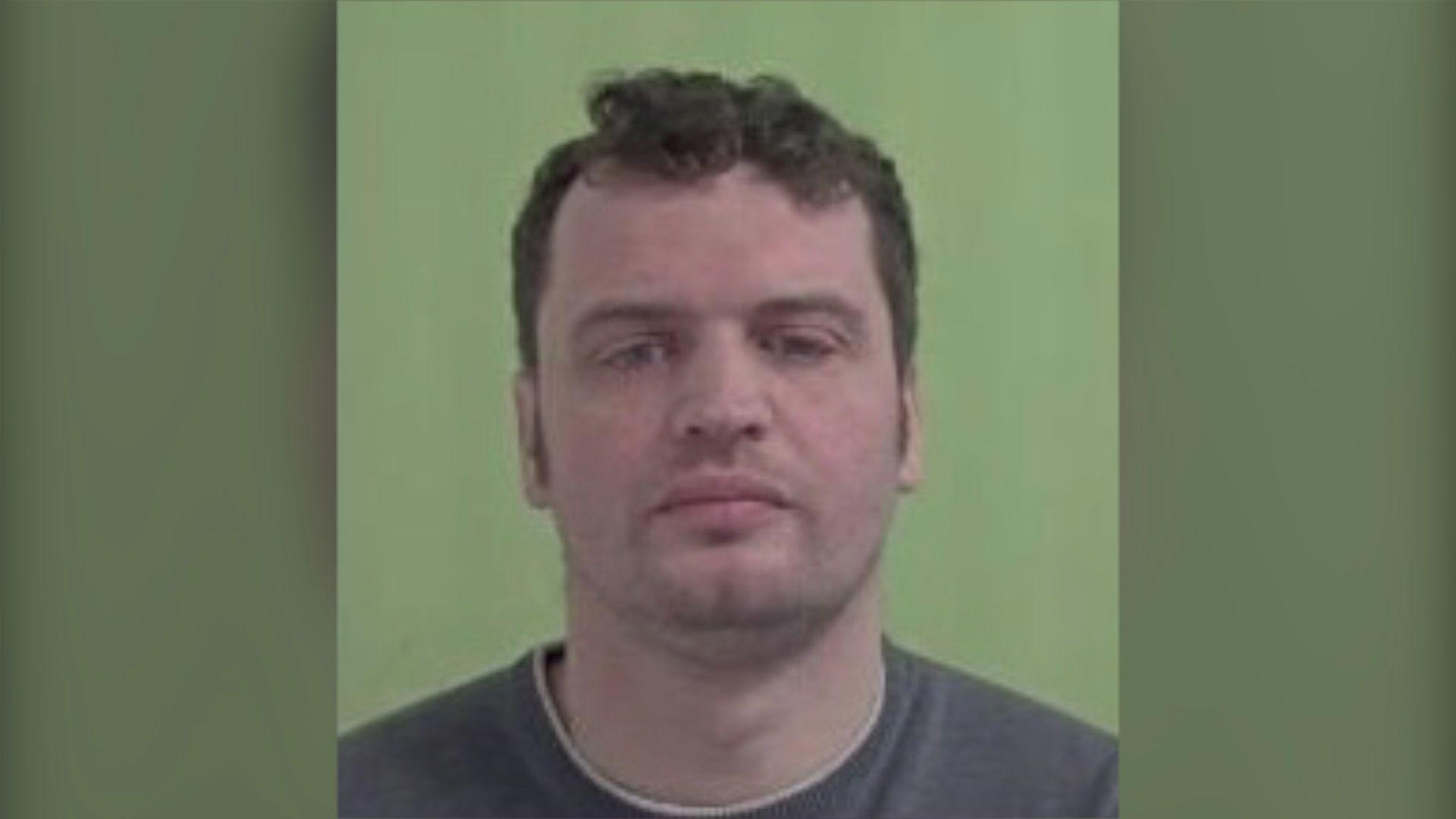 A mugshot of Ashley Harrison, a man with dark hair looks at the camera with a green background.