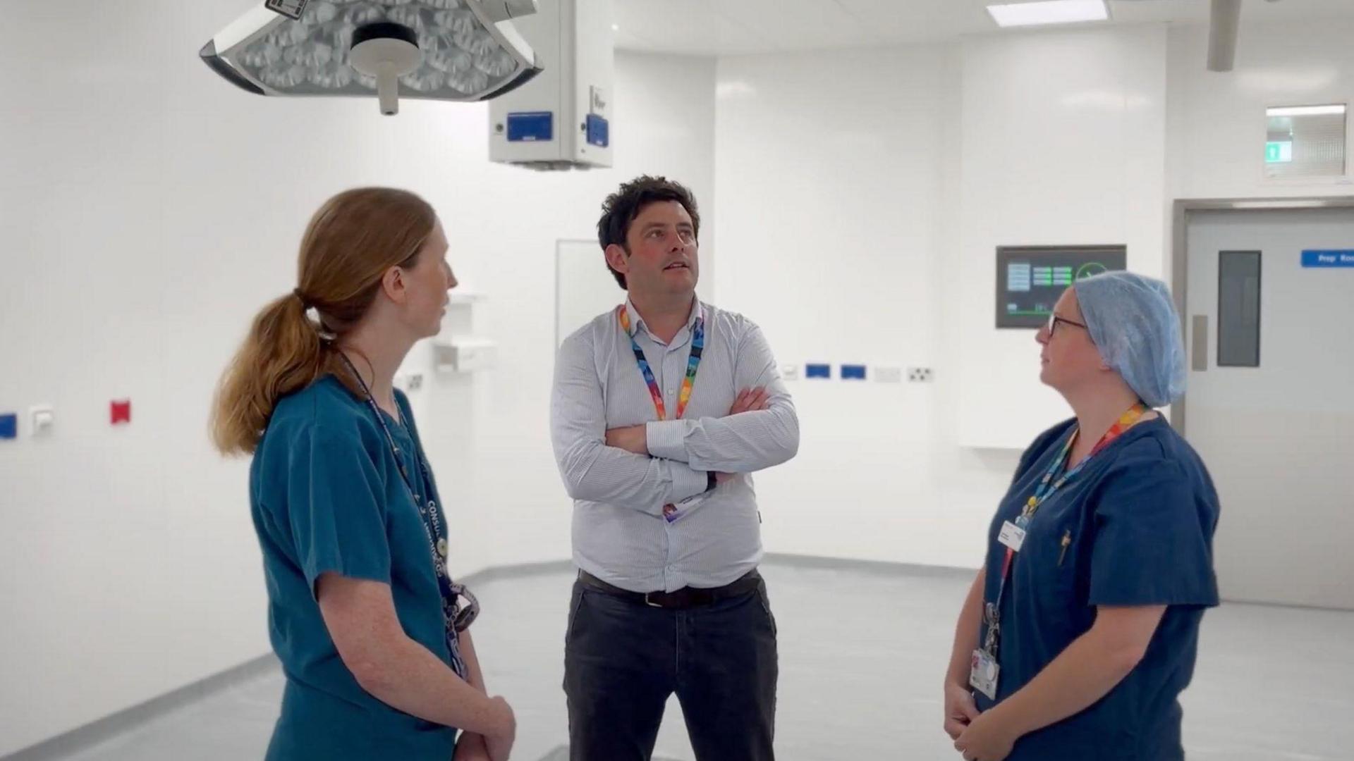 Three members of staff at the hospital stand inside the new operating theatre. Two are in scrubs, and one has a hair net.