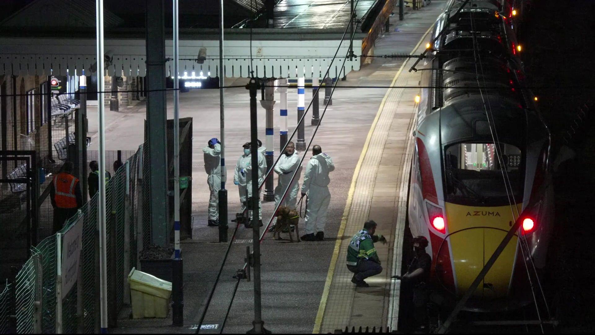A train with people wearing forensic white suits at the station