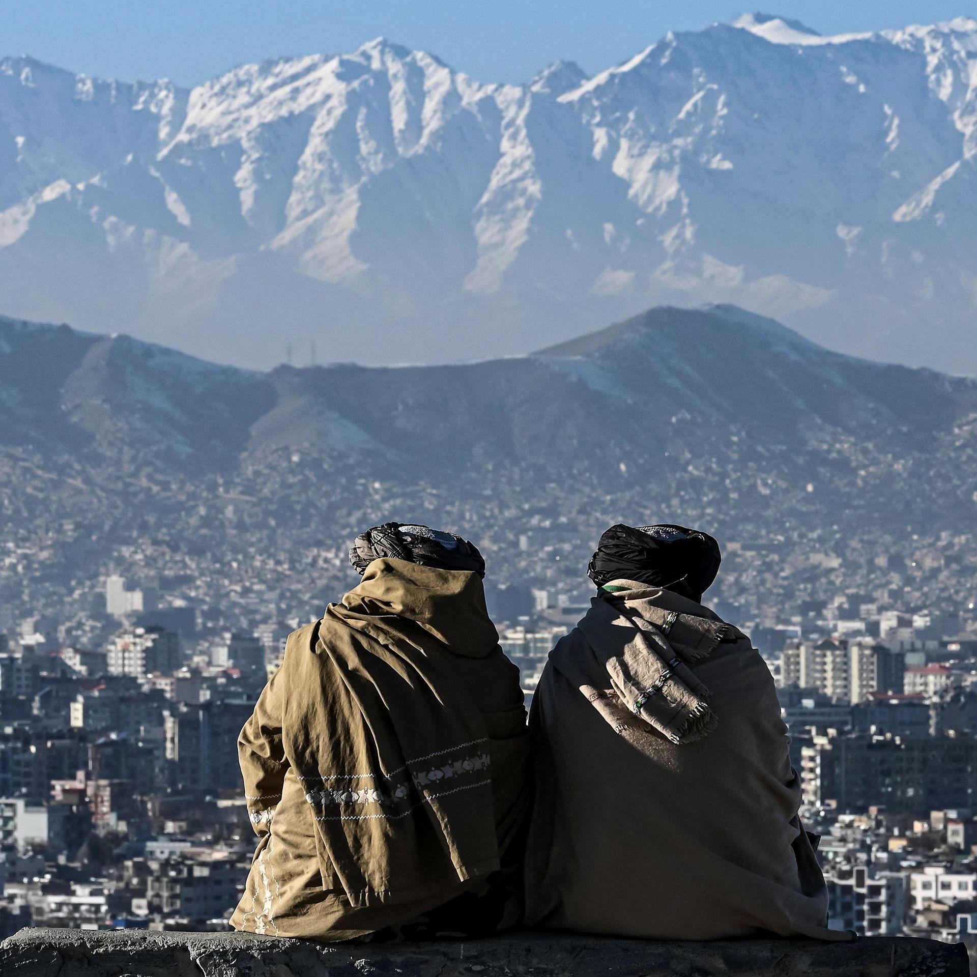 File photo shows two members of the Taliban sitting looking out over the city of Kabul with mountains in the background, they have their backs turned to the camera, taken  at the Wazir Akbar Khan hill in January 2022.