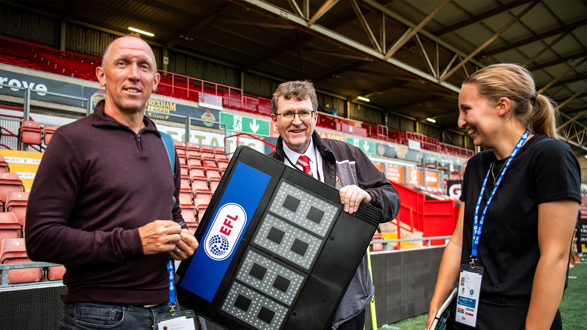 Andy Morrell (left) and Mia Roberts (right) stand either side of Gearint Parry who is holding an electronic substitutes board