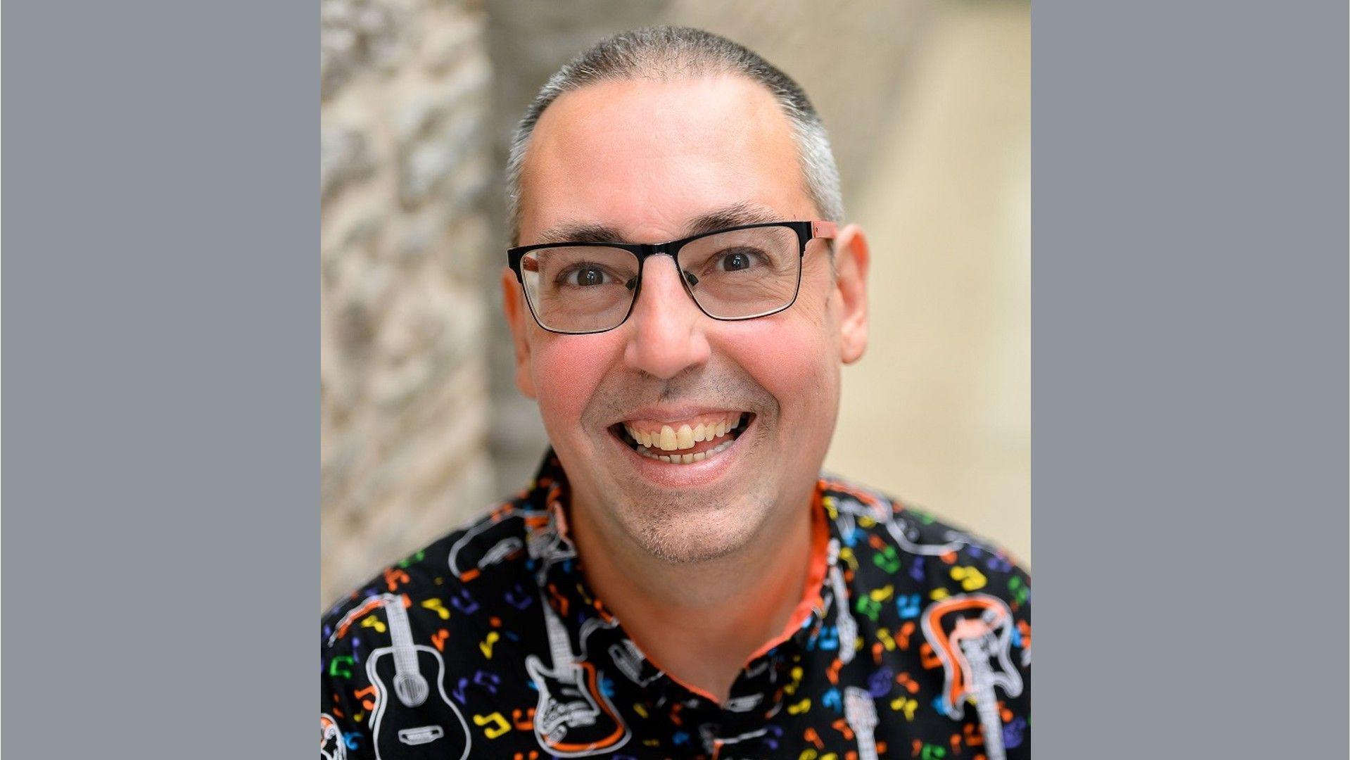 Nailsea Town Council member James Turner smiling at the camera. He is wearing glasses and a colourful shift with guitar motifs on it