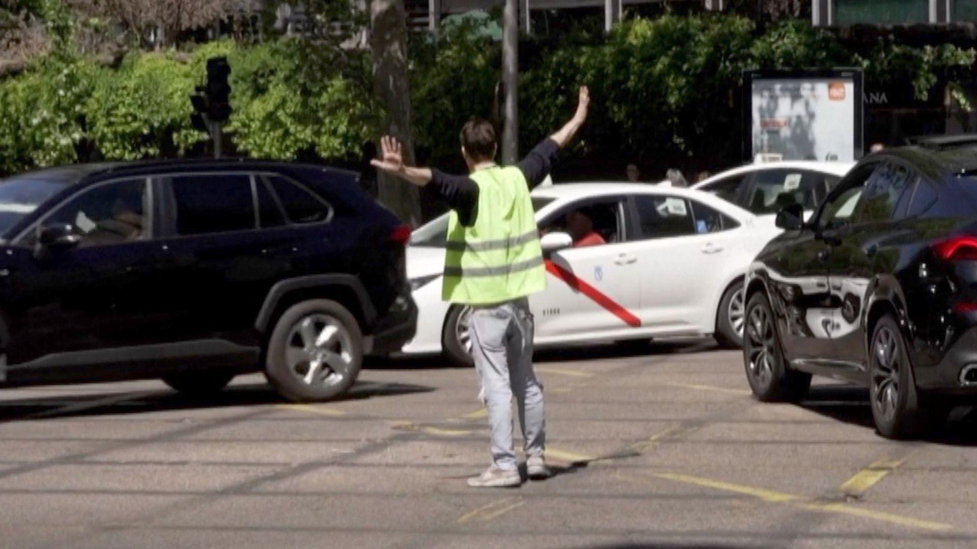 A man in a high-visibility jacket is directing traffic in the middle of the road, cars are passing him