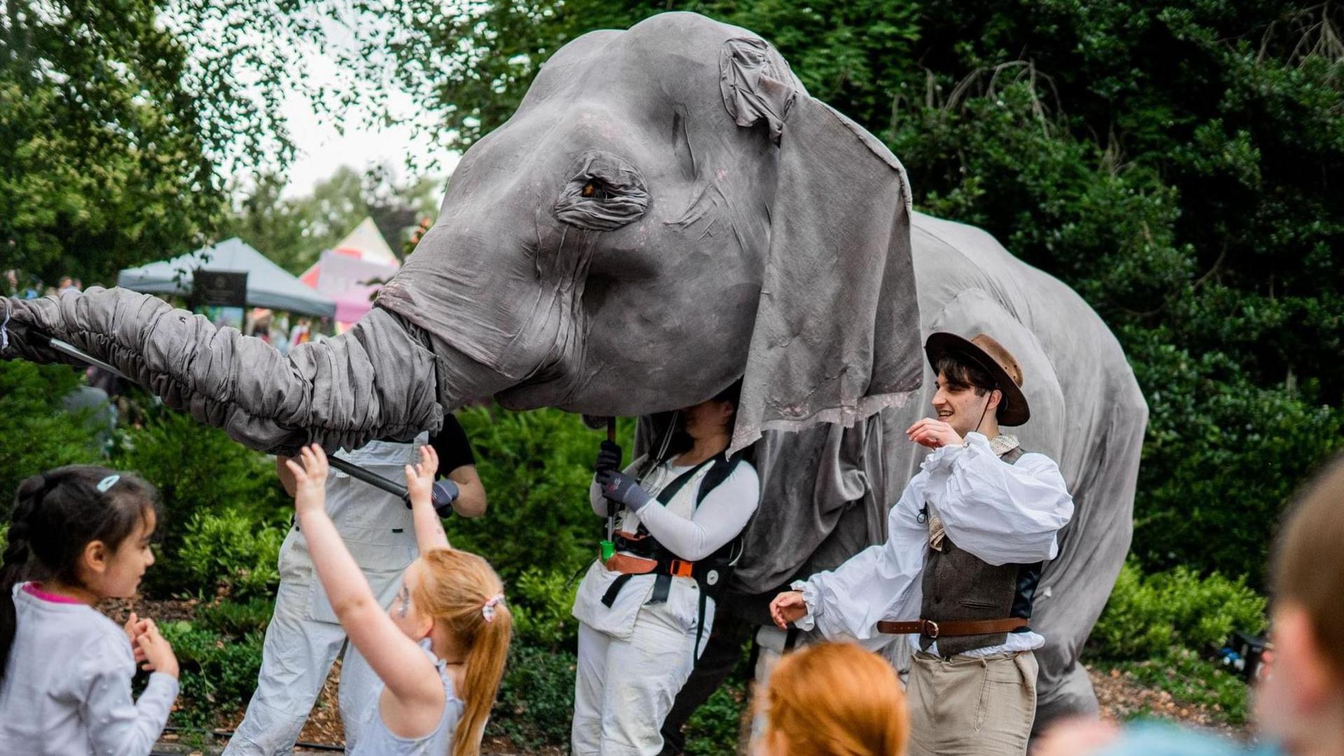 A life-sized grey elephant puppet being controlled by a group of puppeteers through Bath Carnival