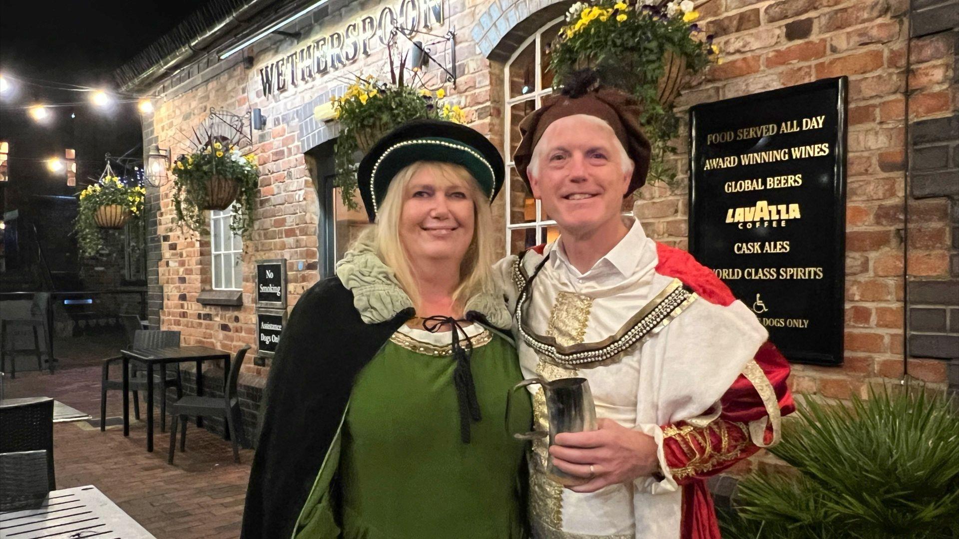 Two people dressed in medieval clothing halfway through the 'Assize of Ale' tradition in Gloucester Docks.