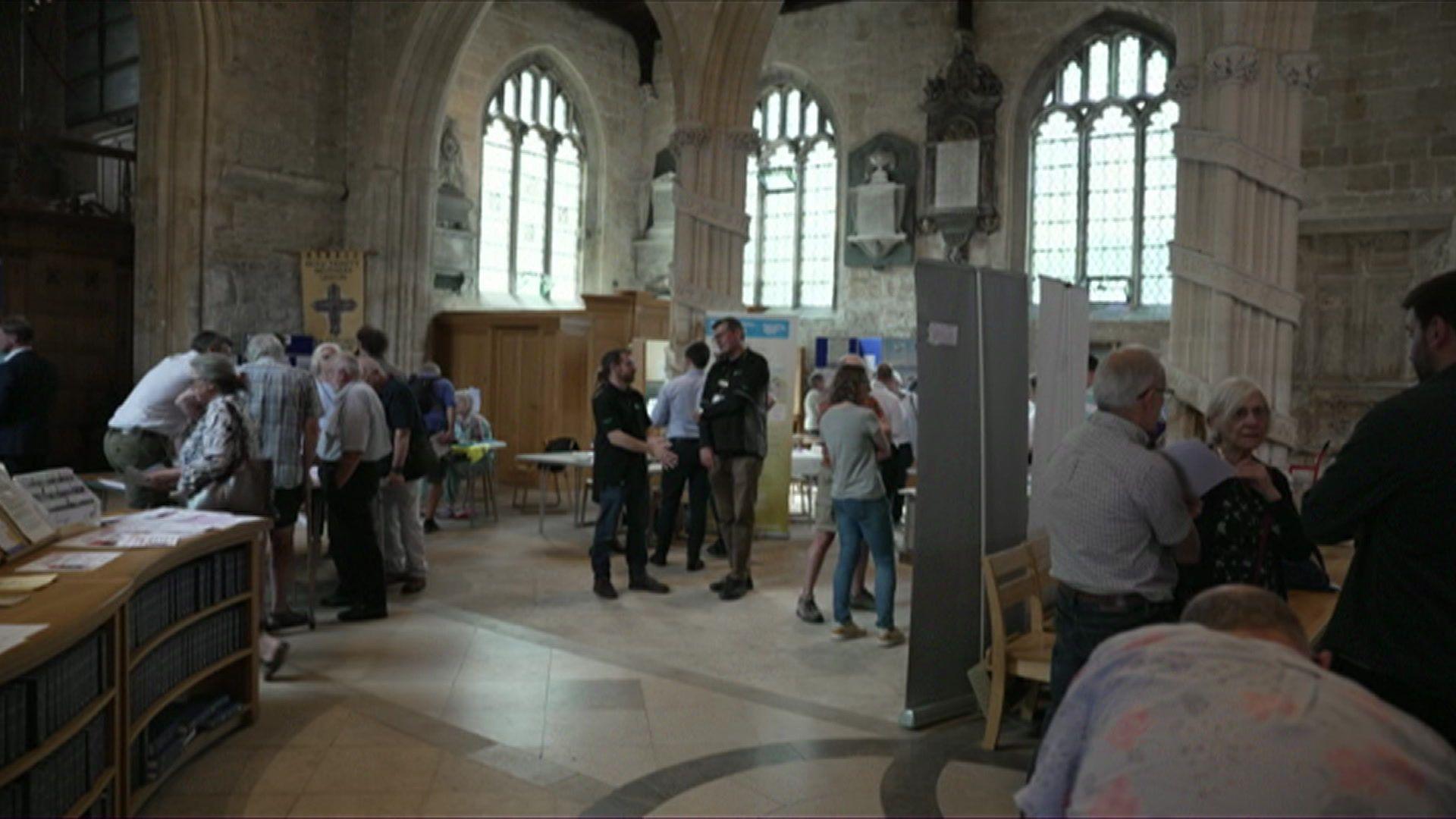 People gathering in a church, standing talking to one another, with lots of large banners around with information