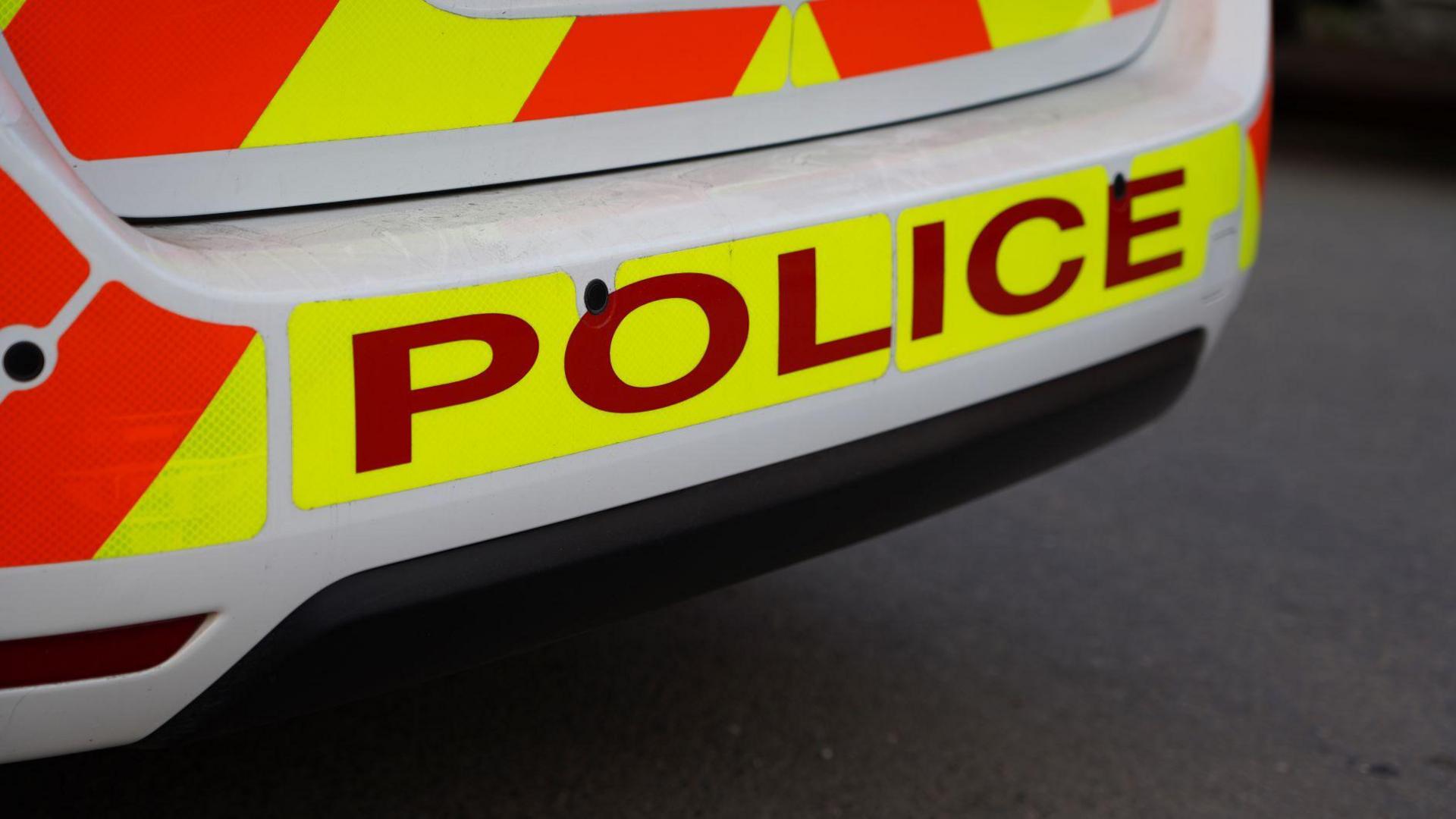 A close up of the back of a police car. The words "Police" are written in red lettering on neon yellow background.