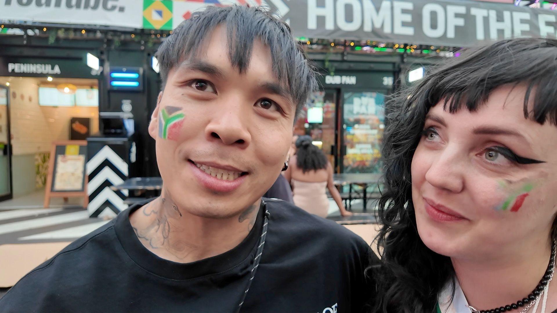 A man and a woman stand in Croydon's Box Park, each with a South African flag painted on their cheek.