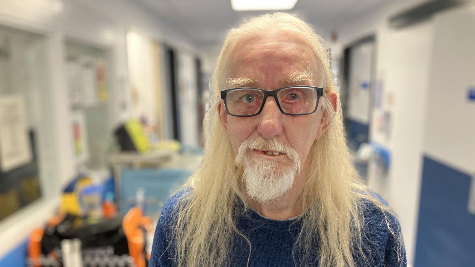 Leon Farmer inside a hospital. Mr Farmer has long hair and wears glasses. He is looking at the camera.
