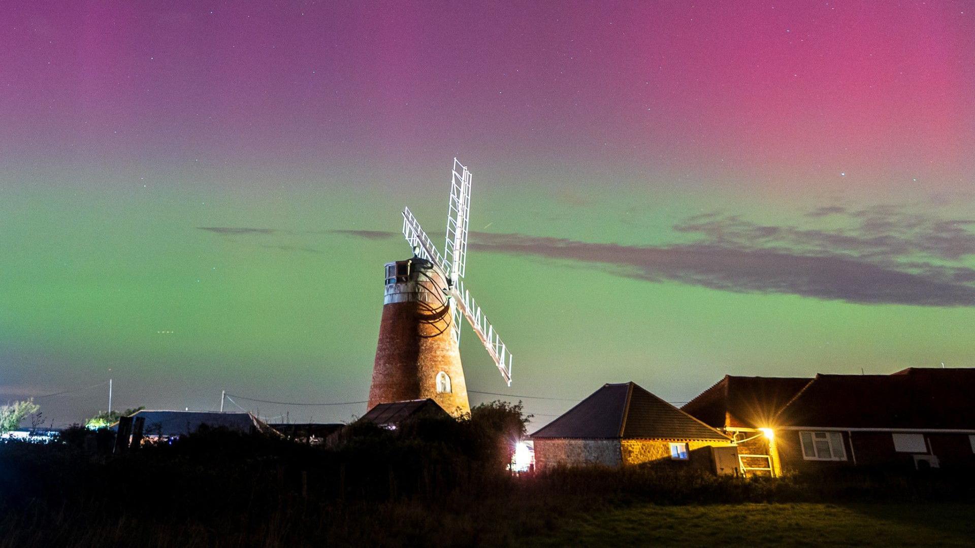 A windmill at night as the sky is illuminated pink and green. 