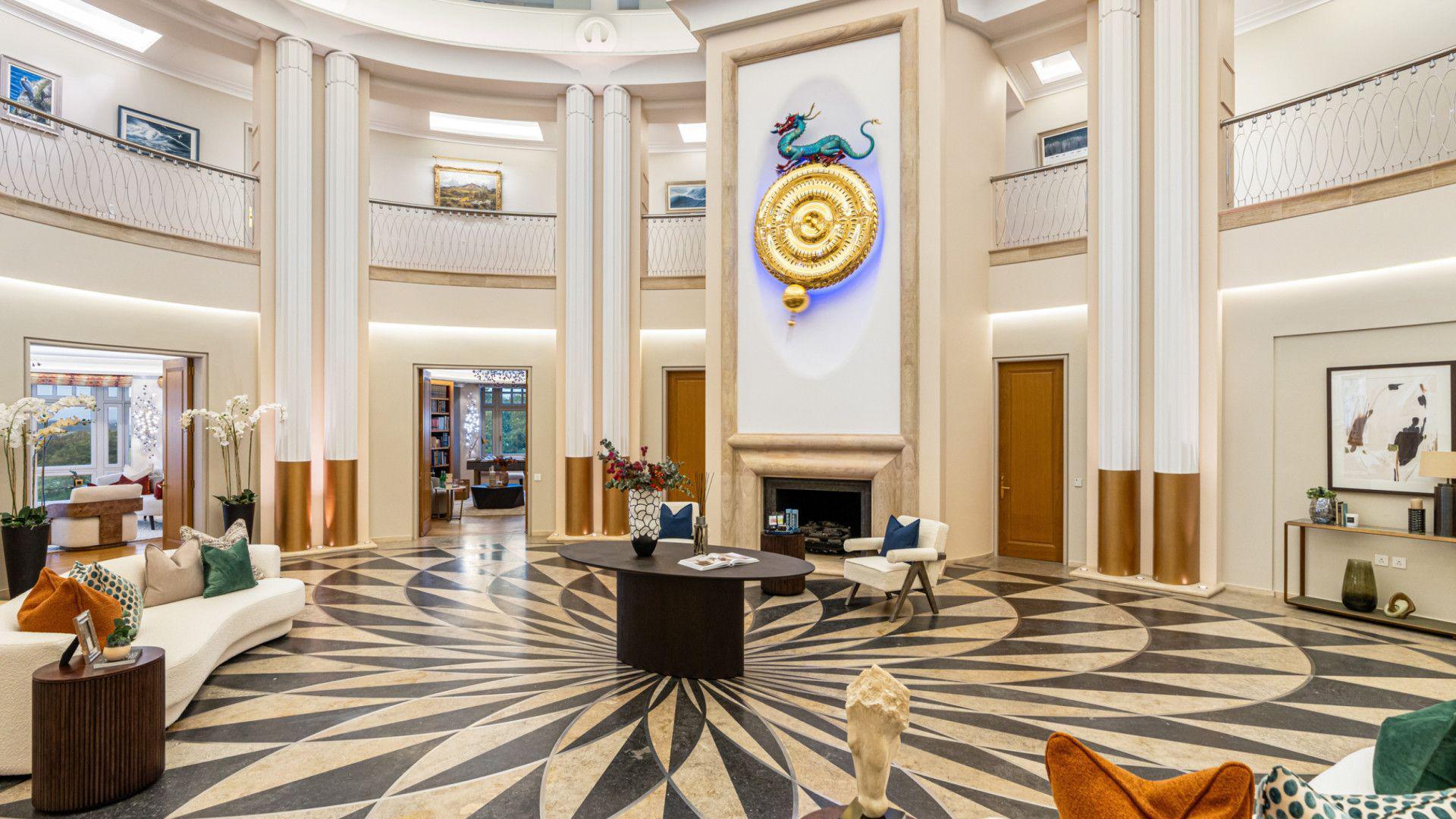 The large atrium with a balck and white patterned floor and a large time piece with a dragon design on top in on a wall the far wall. There are balconies surrounding it.