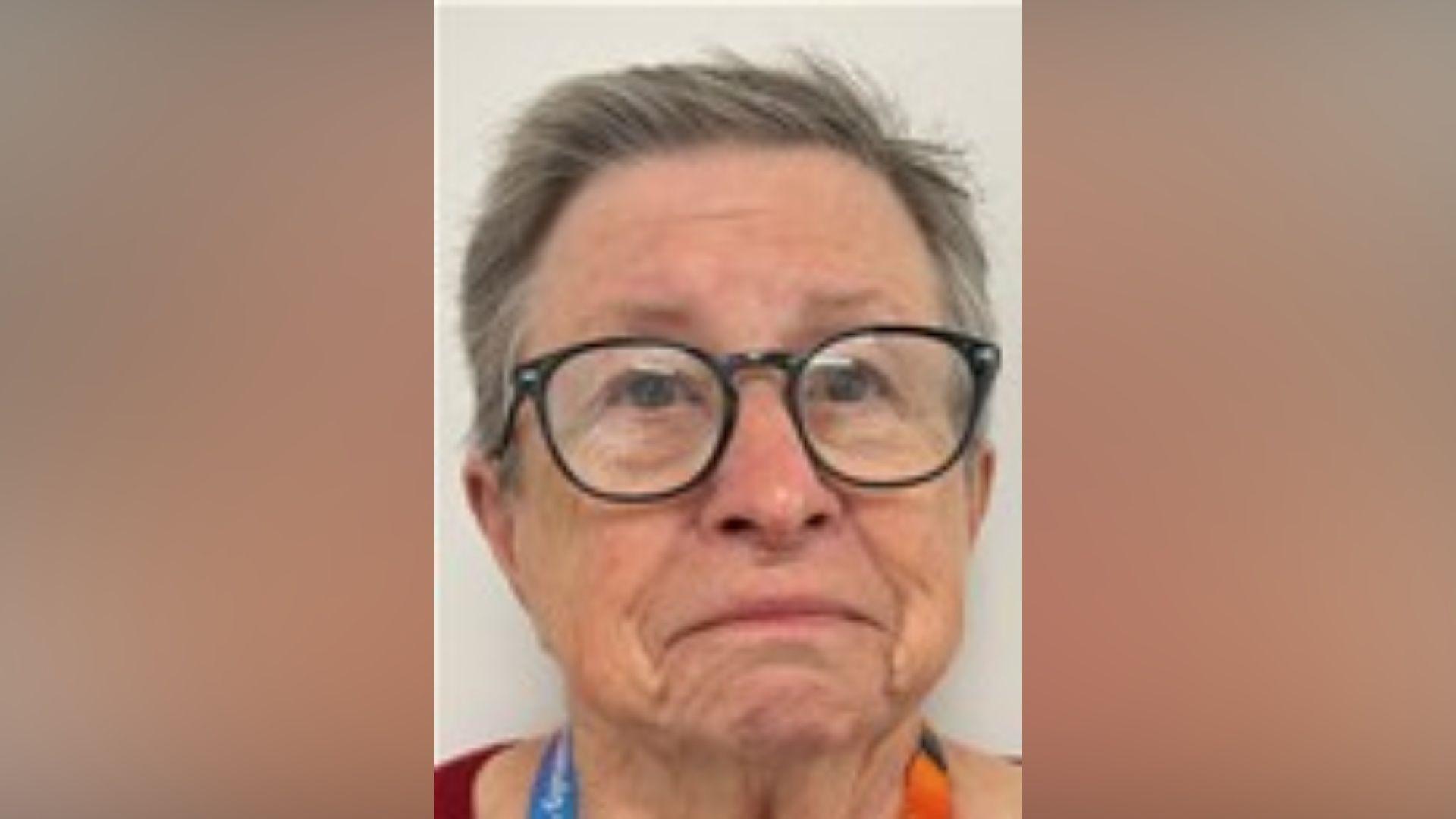 A woman wearing glasses is looking directly at the photographer. She has short grey hair and is wearing a lanyard.