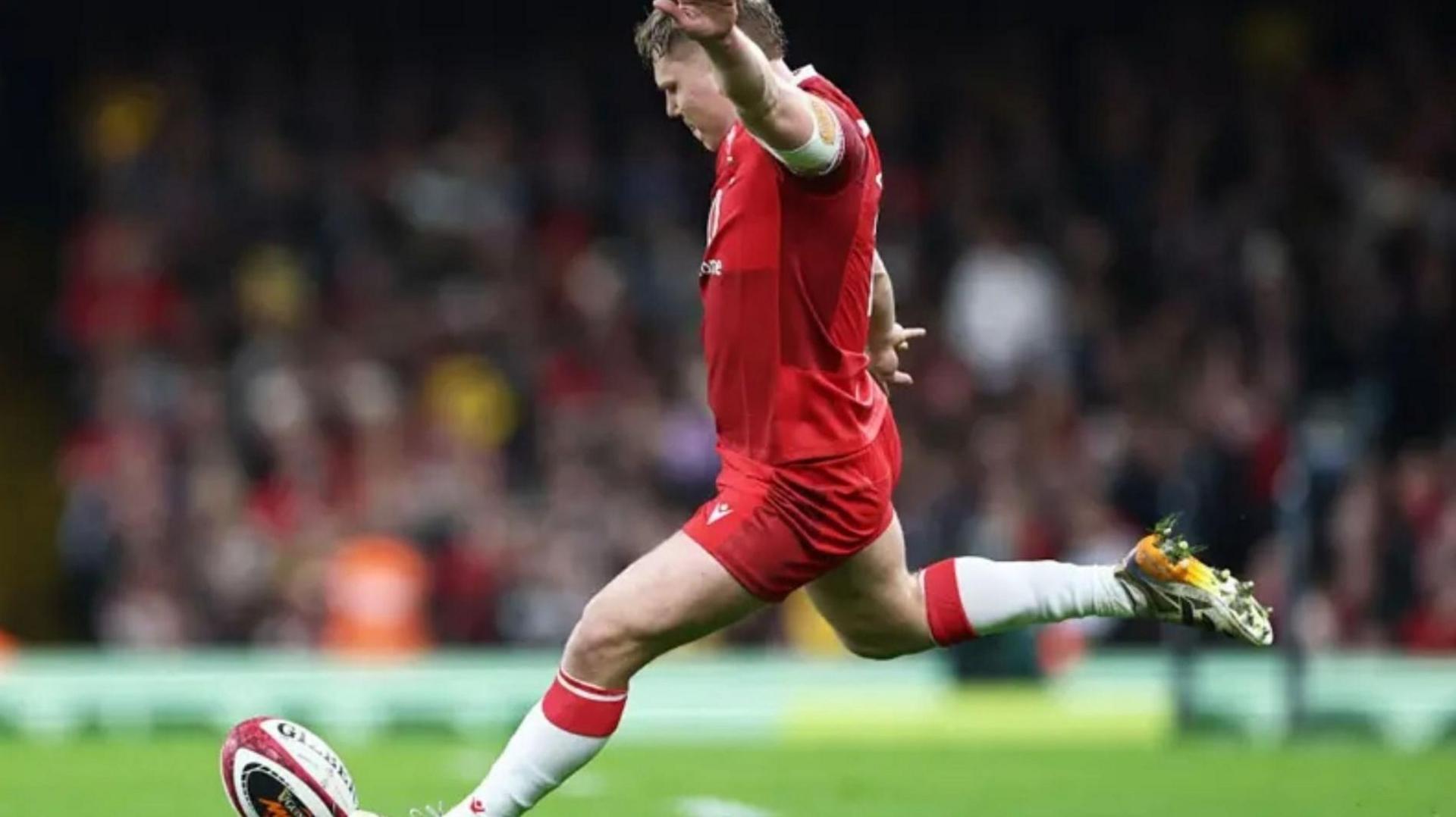 Llun o Sam Costelow yn cicio pel yn ystod y gem