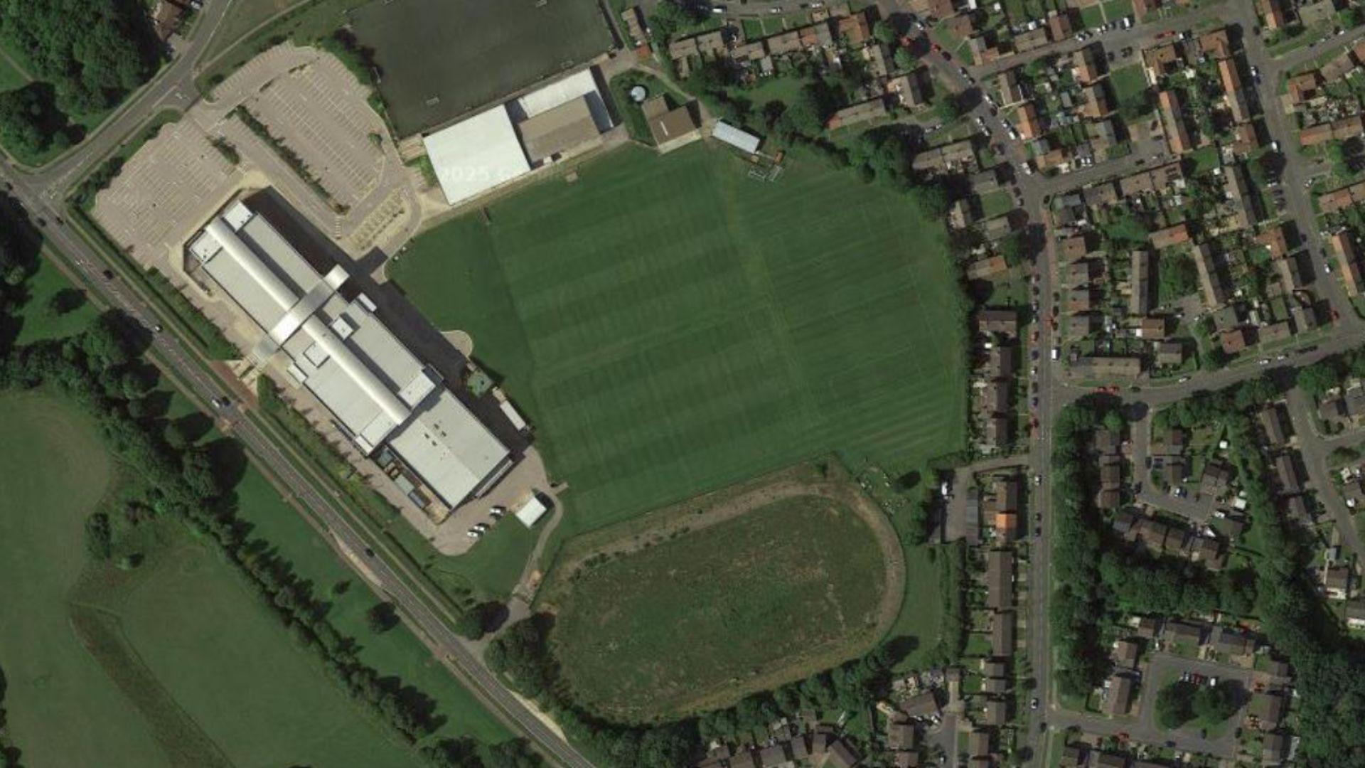 A Google Maps image showing an aerial view of the proposed site. A college building stands to the left of neatly but fields. Below them is the disused running track which is unkempt.