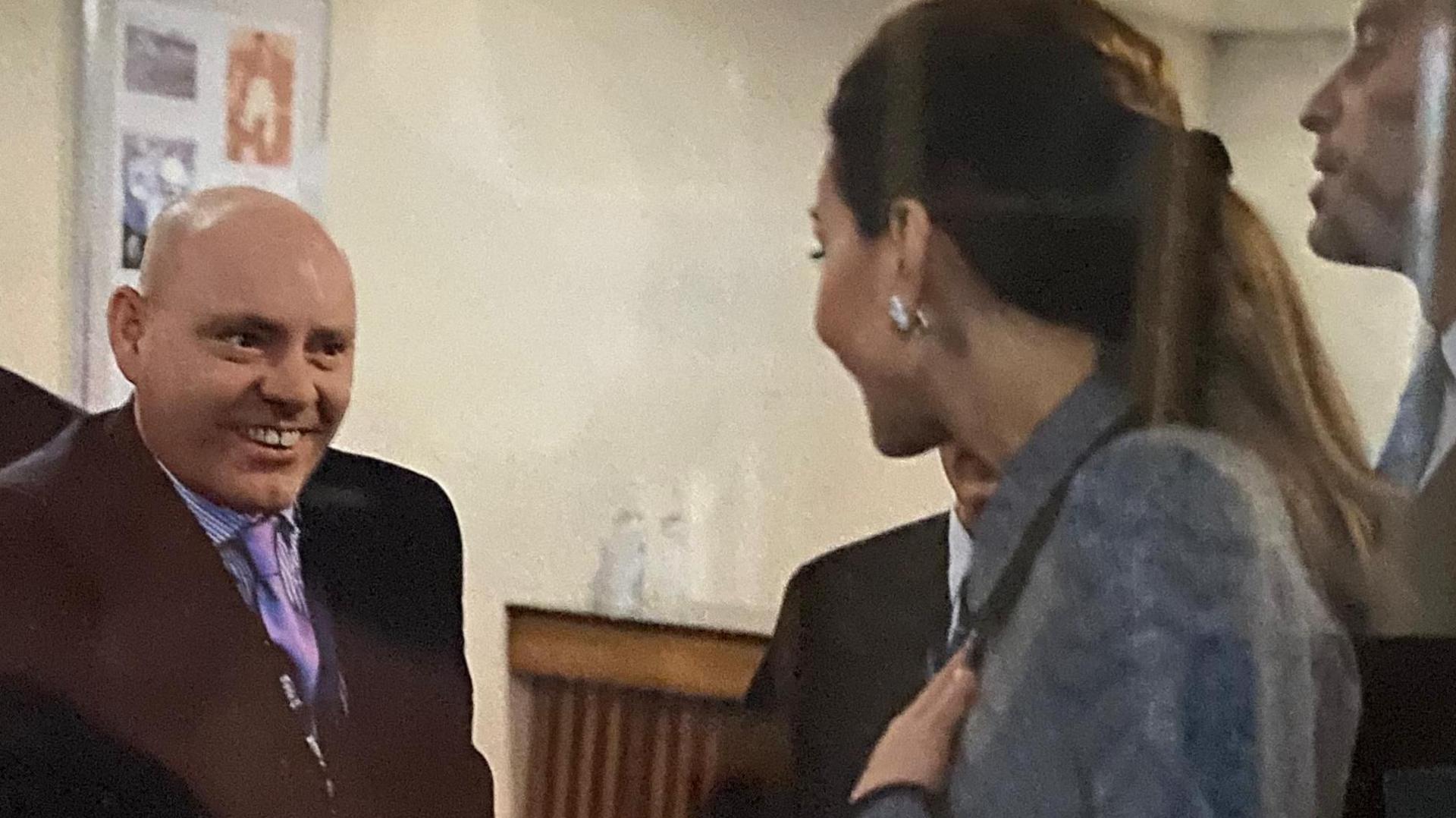 A smiling man in a suit shaking the hand of Kate Middleton