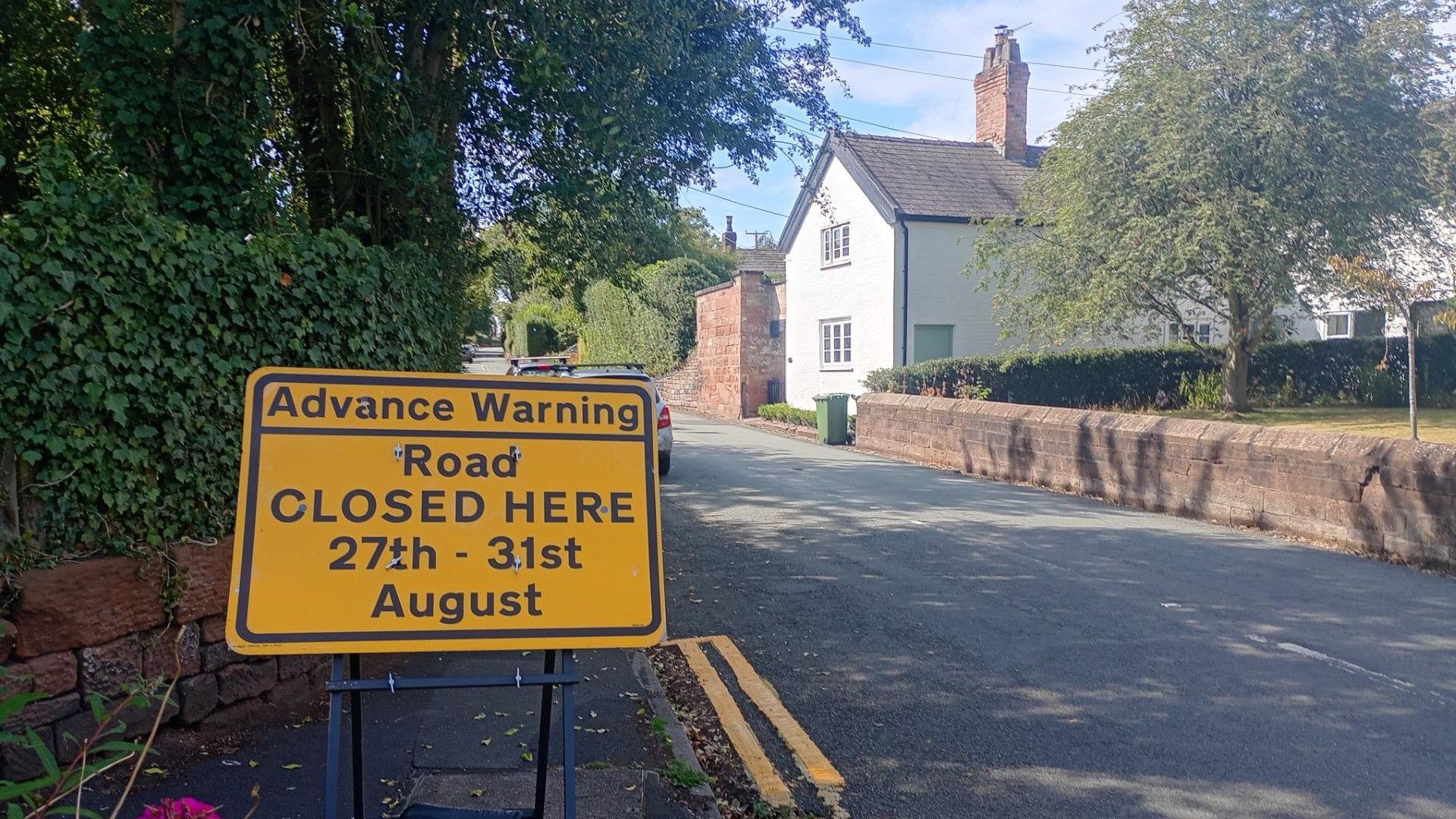 A yellow road sign warning of a road closure between 27-31 August