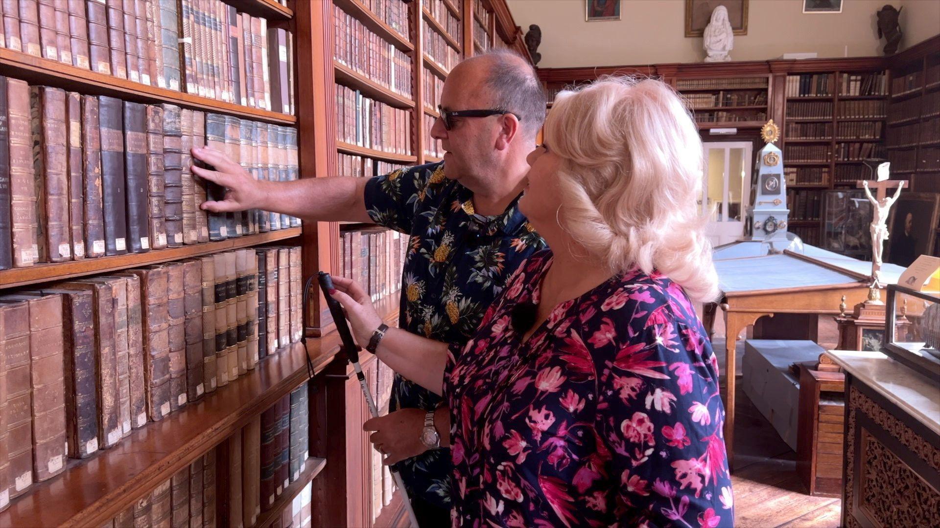 Debbie Ramsey and Daren Smith in the museum at Stonyhurst College. Daren is feeling books on a shelf while Debbie stands next to him.