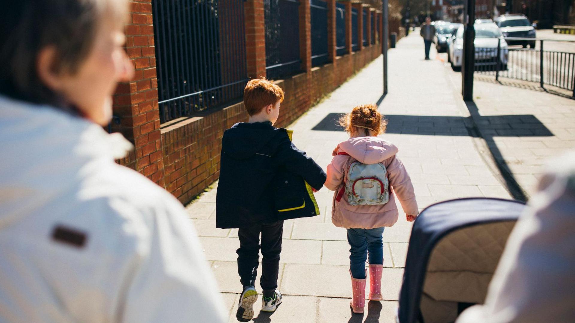 A family walk along a footpath with parent pushing a pram and grandparent alongside. The two children are dressed in jackets and denim jeans.