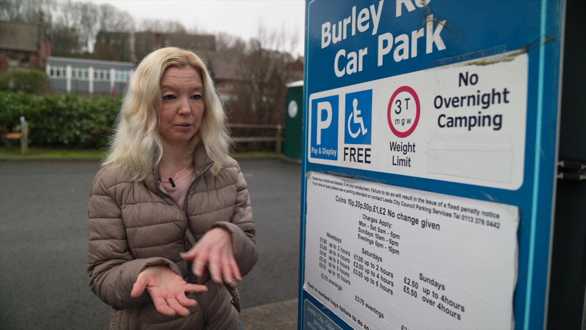 Woman with blonde hair stands next to a parking board