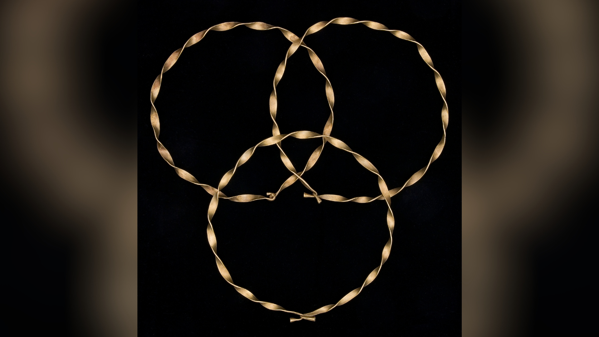 Gold bracelet-sized rings partially placed on top of one another, pictured against a black backdrop