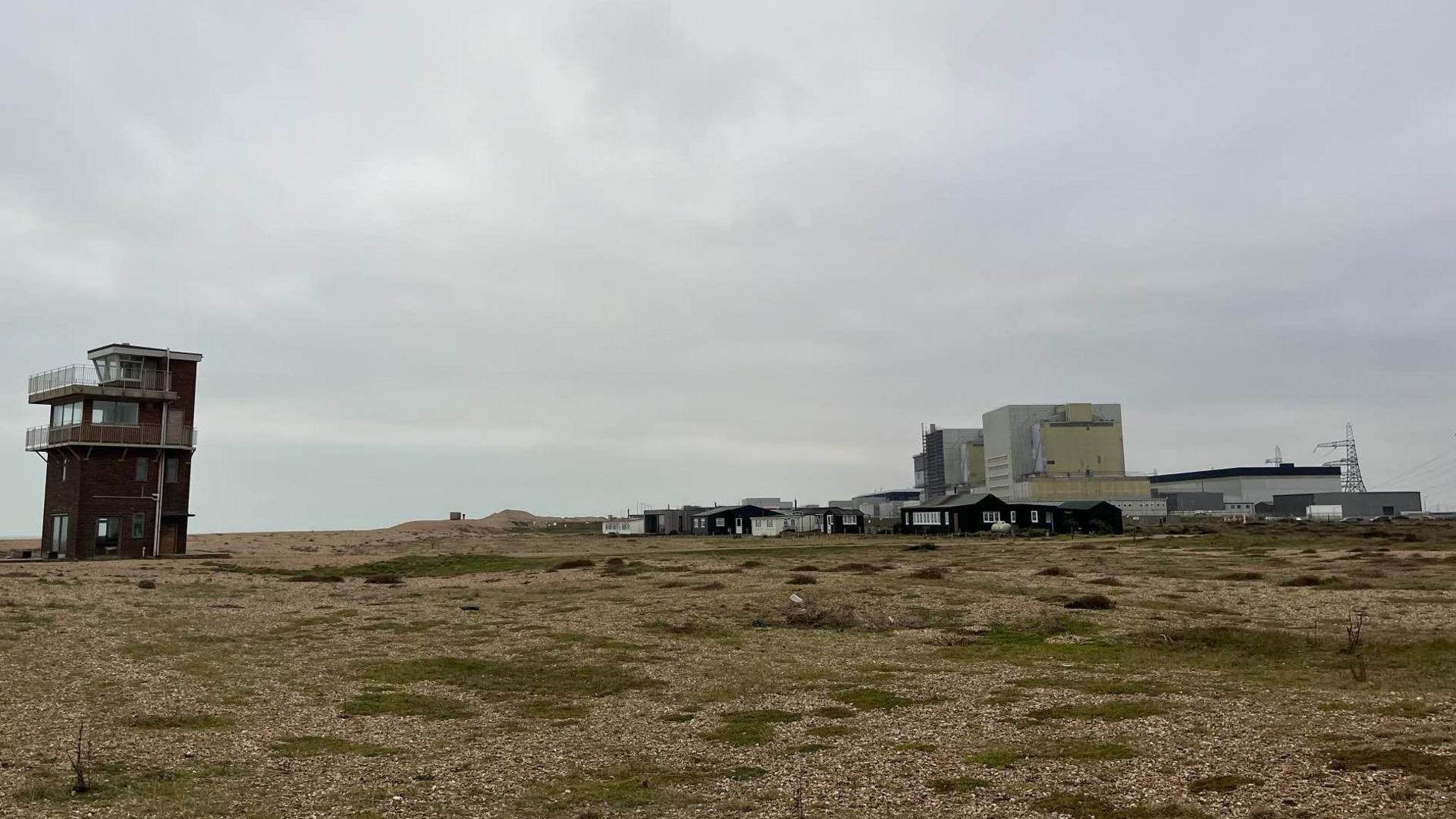 Coastguard lookout station on Dungeness beach with a nuclear power station in the background and a shingle beach in the foreground.