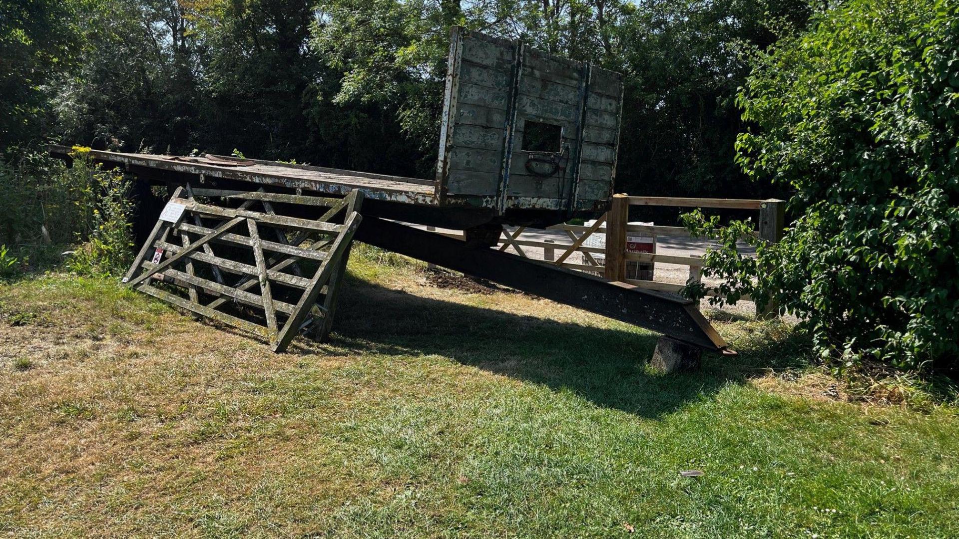 A detached farm trailer positioned in front of the gates to the field, with a couple of removed gates lent against the trailer. 