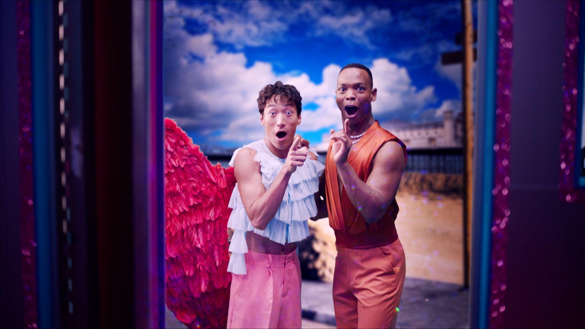 Two dancers look excited and point towards the camera, about to get on a party bus.