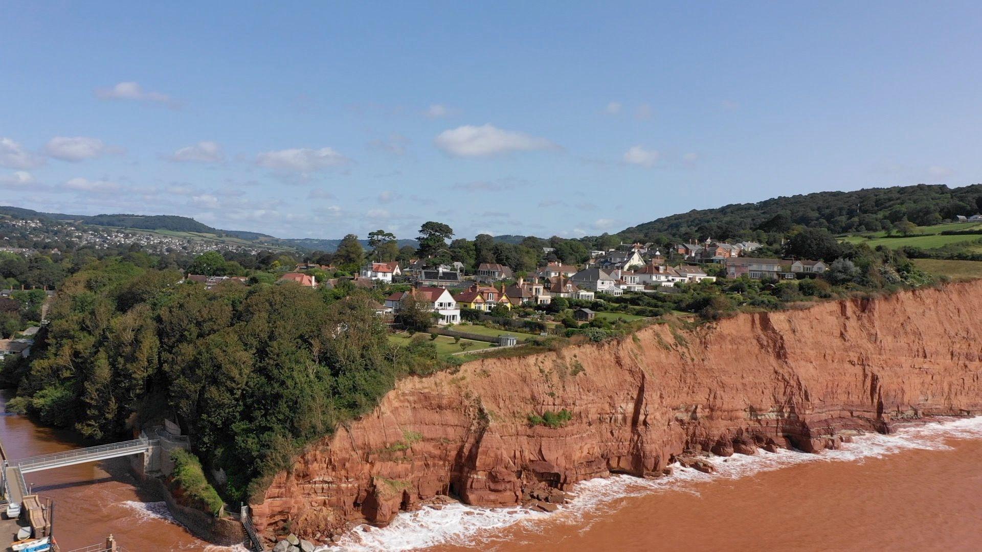 Cliffs at Sidmouth's East Beach, which are coloured a brown-red and have a number of properties on top