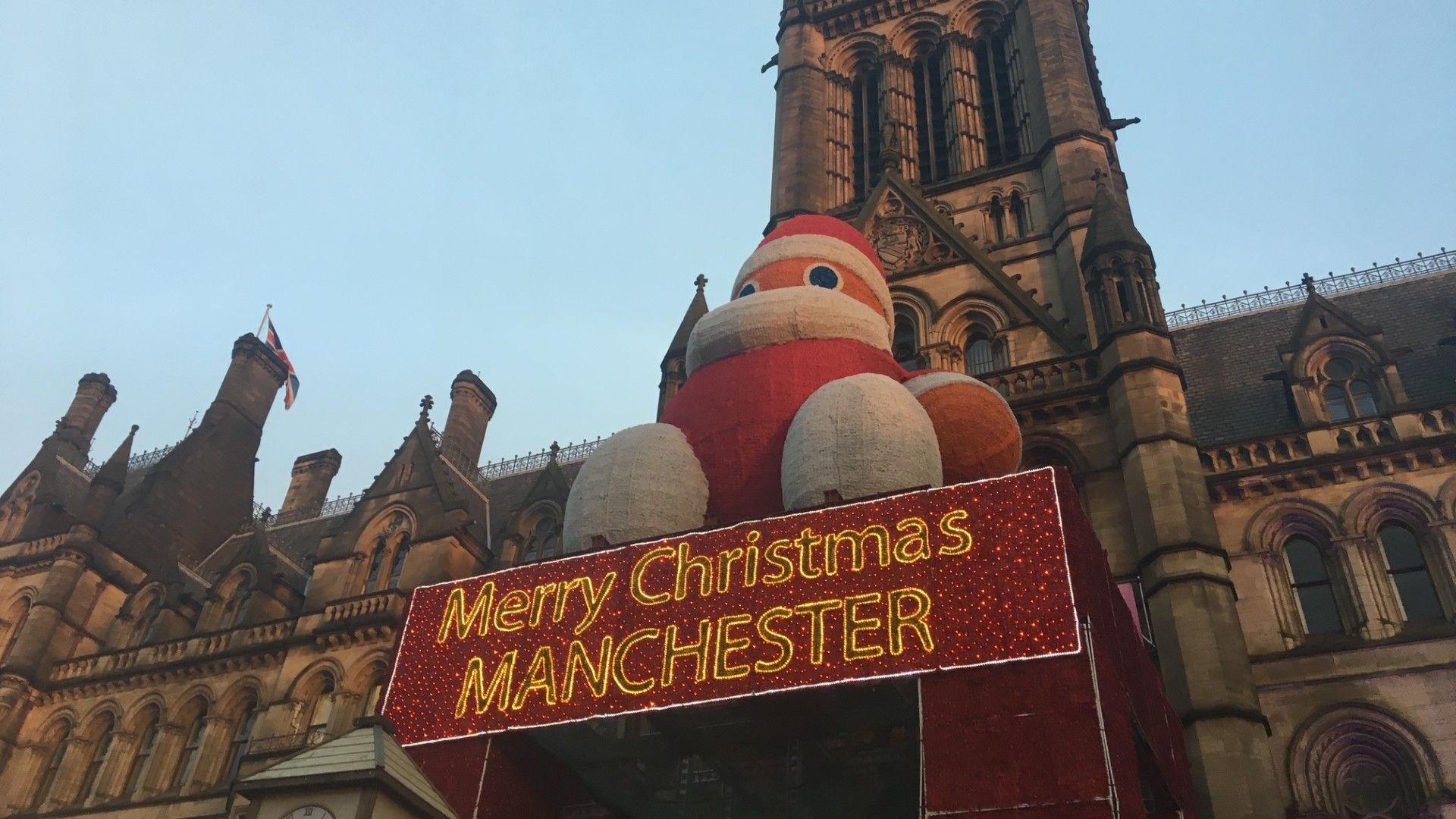 A giant Father Christmas sits on top of a red sign that reads 'Merry Christmas Manchester'