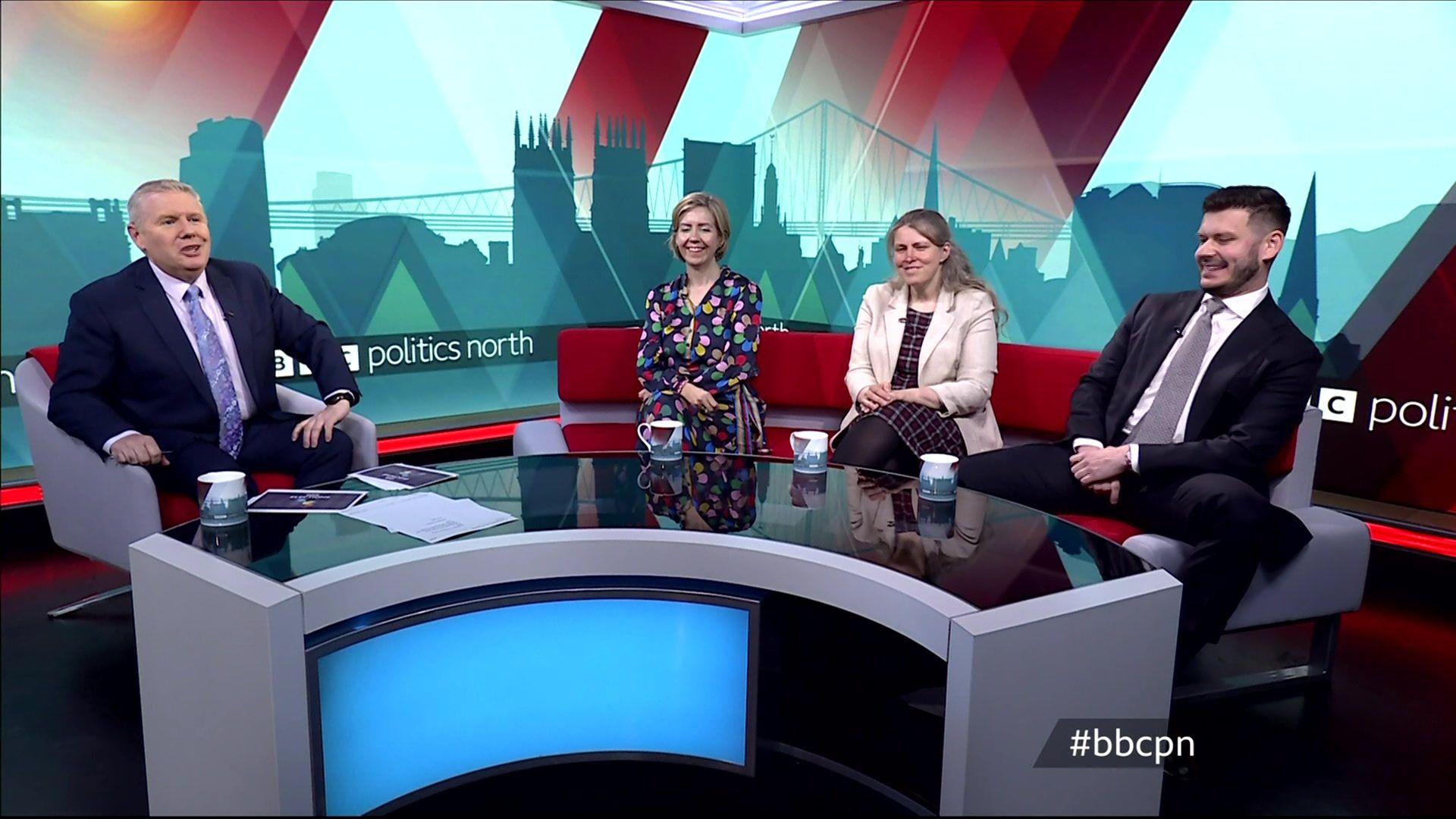 Tim and the three politicians sit on a curved sofa around a curved desk in the BBC red branded colours. Politics north is on a strap-line across the set at the back.