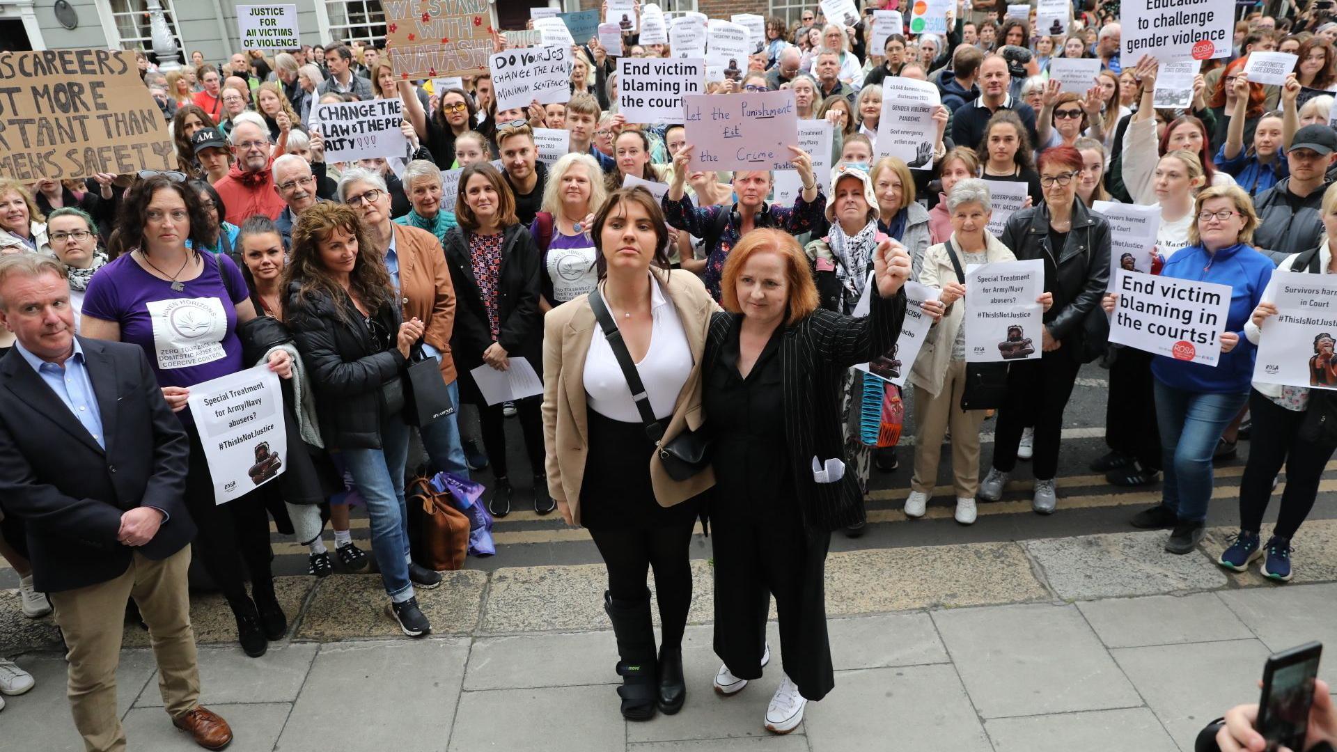 Two women, backed by a crowd holding placards and signs, protest against the sentence of a man convicted for an assault on Natasha O'Brien. 