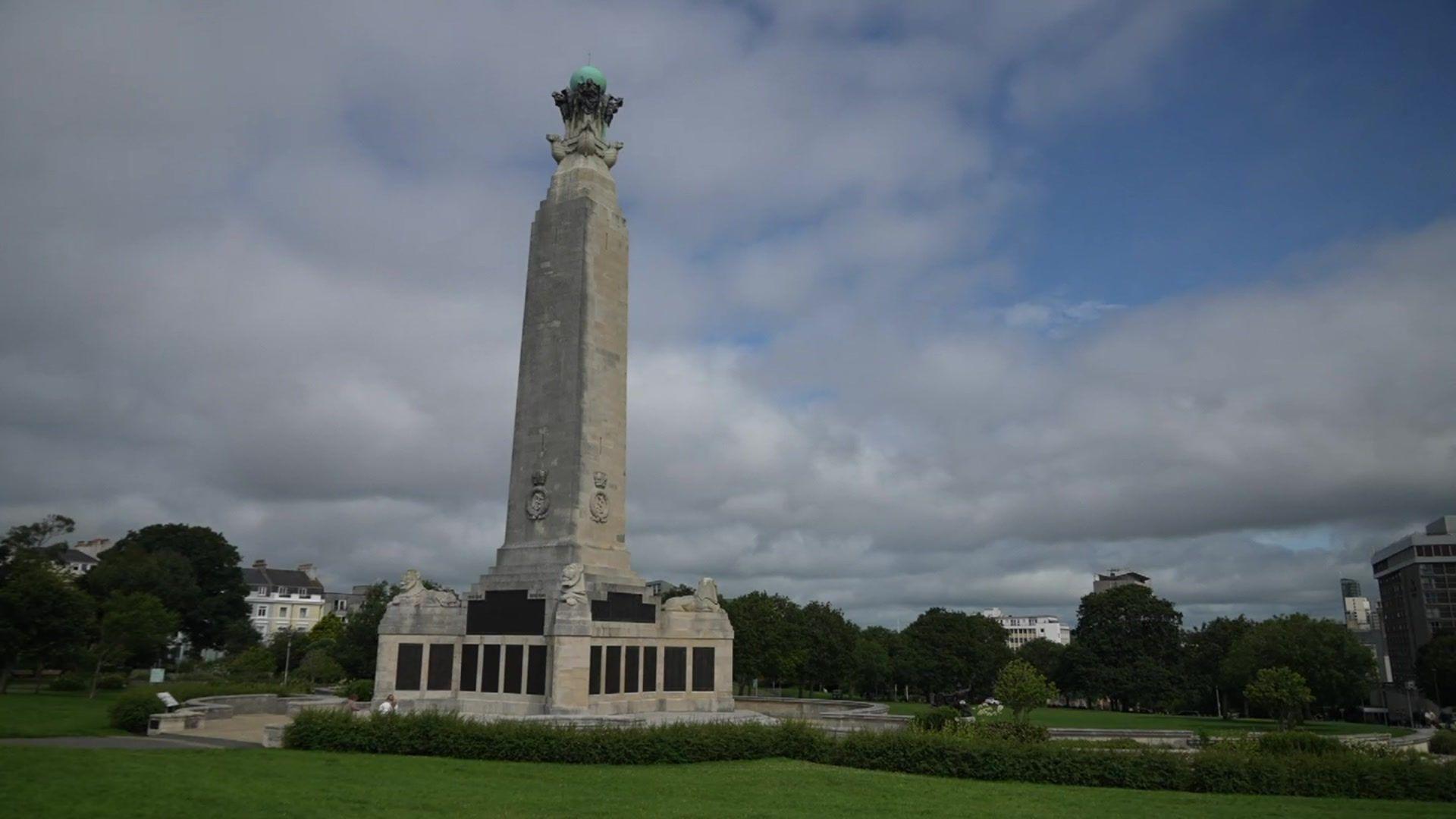 Blue skies and clouds of memorial spire which rises above plaques showing the names of those who lost their lives 