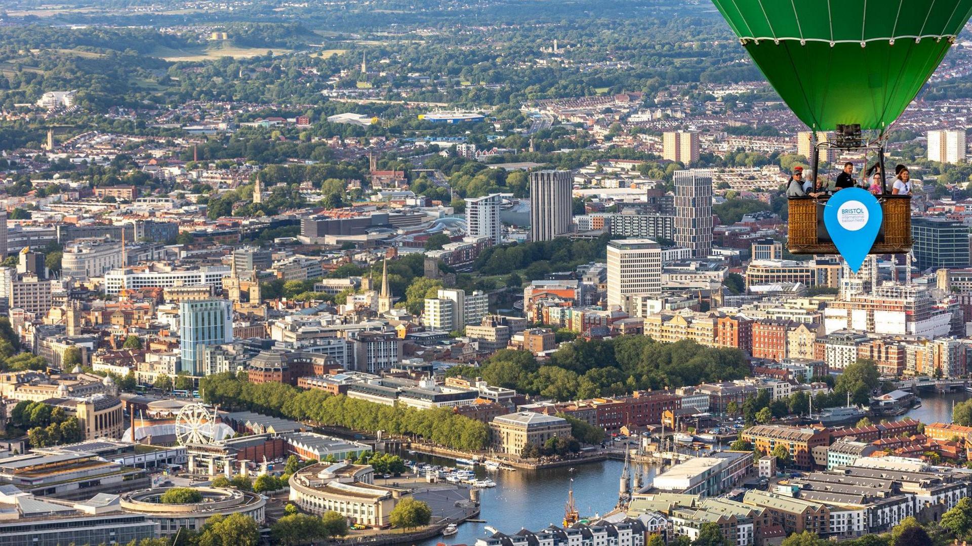 A hot air balloon flies over the centre of Bristol with the harbourside visible below