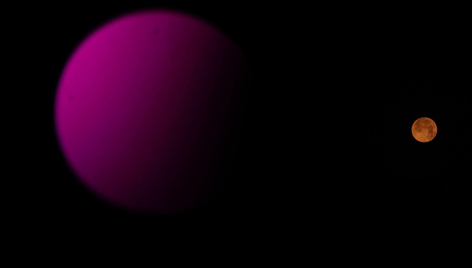 A large purple circle is seen in the foreground, with the orange Moon much smaller against a starless night sky in Delhi on Wednesday.