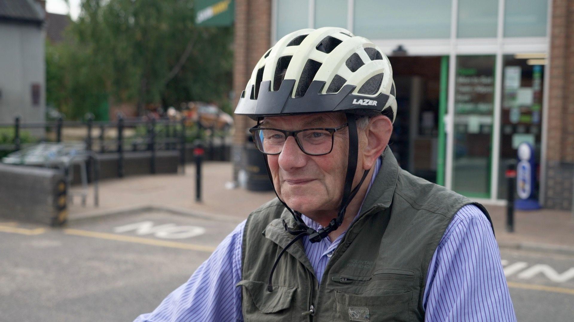 A man wearing glasses and bicycle helmet in front of a building which has its green-framed door open.