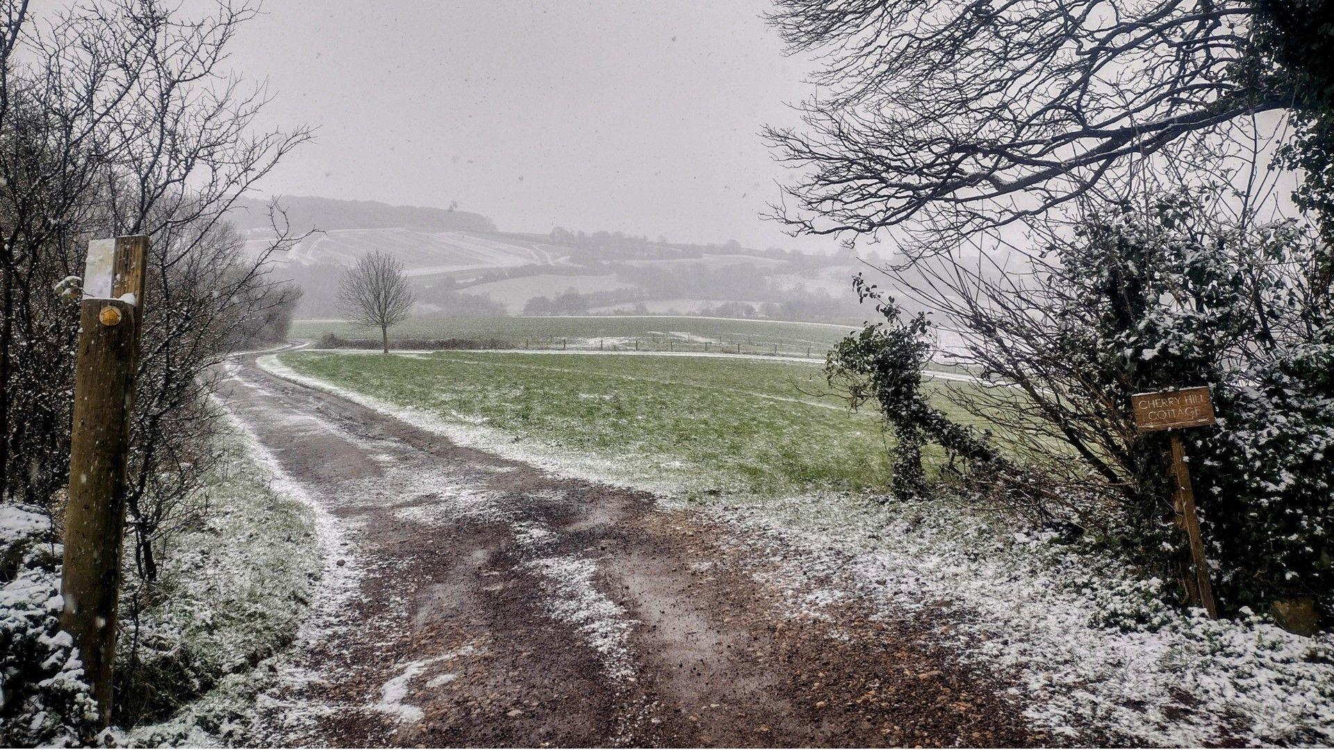 Rural view of farm track and rolling green fields covered in a light dusting of snow