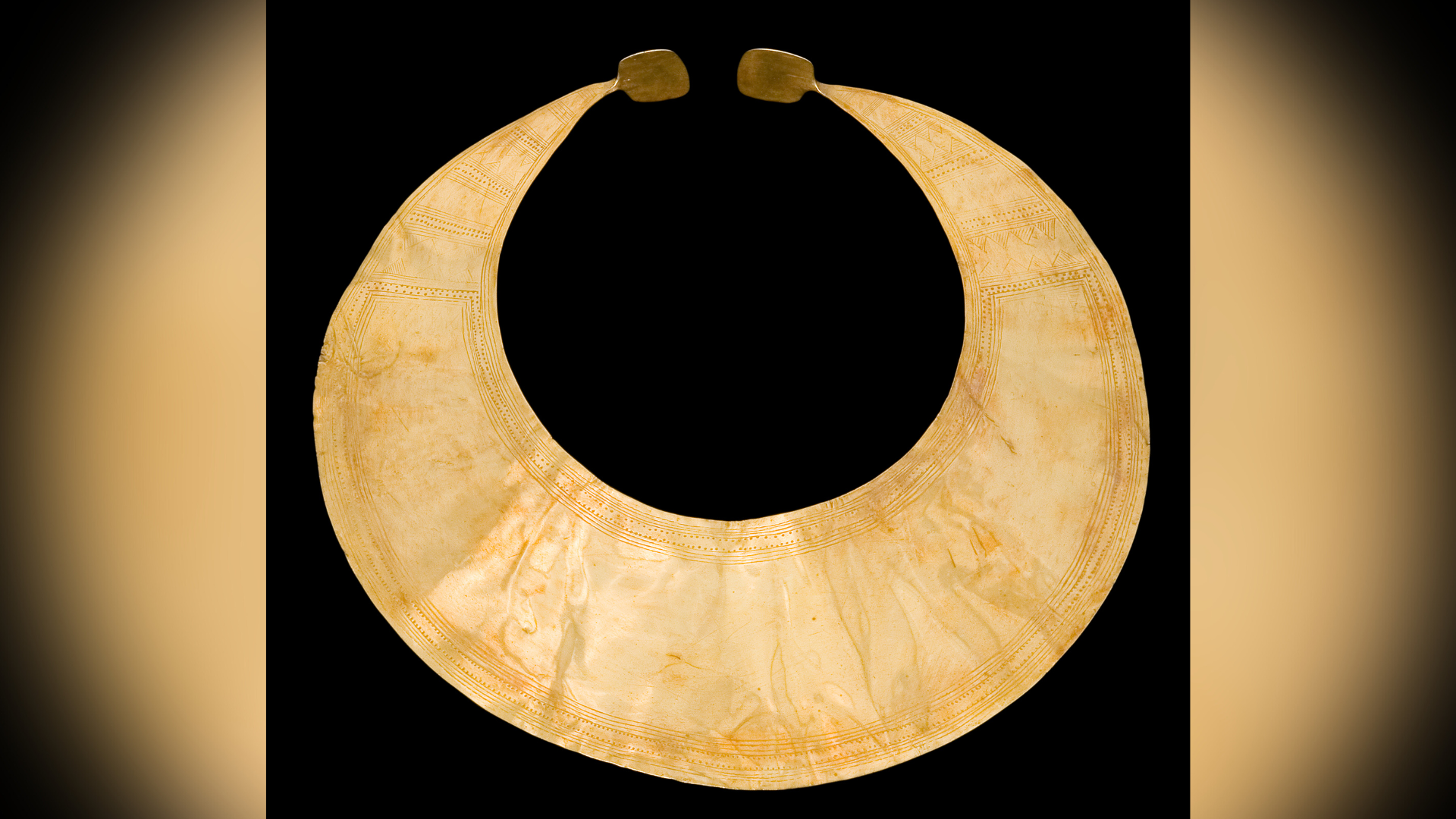 A gold crescent shaped lunula is pictured against a black backdrop.