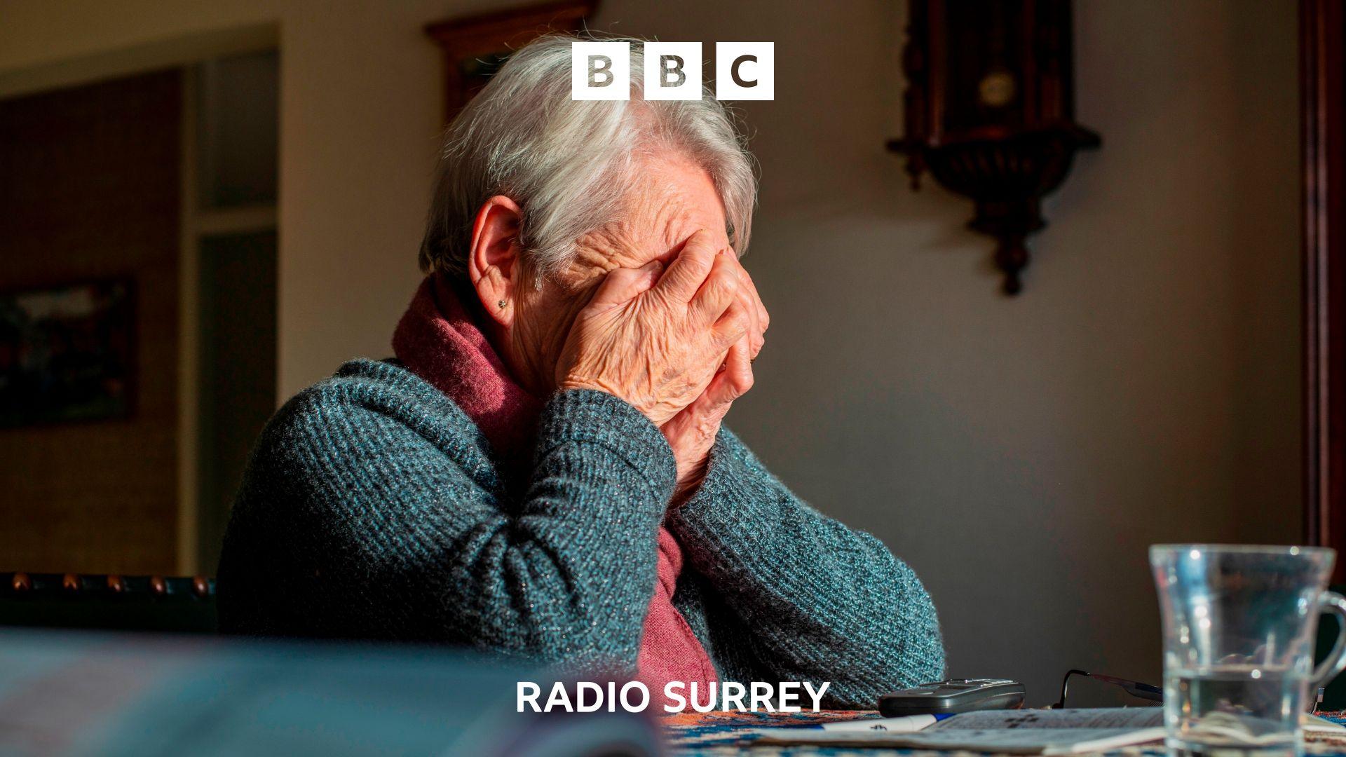 An elderly woman sits with her head in her hands.