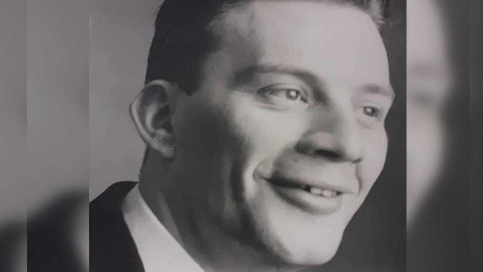 A black and white photo of Anthony Scarrott. He is facing sideways and is wearing a suit and a shirt.