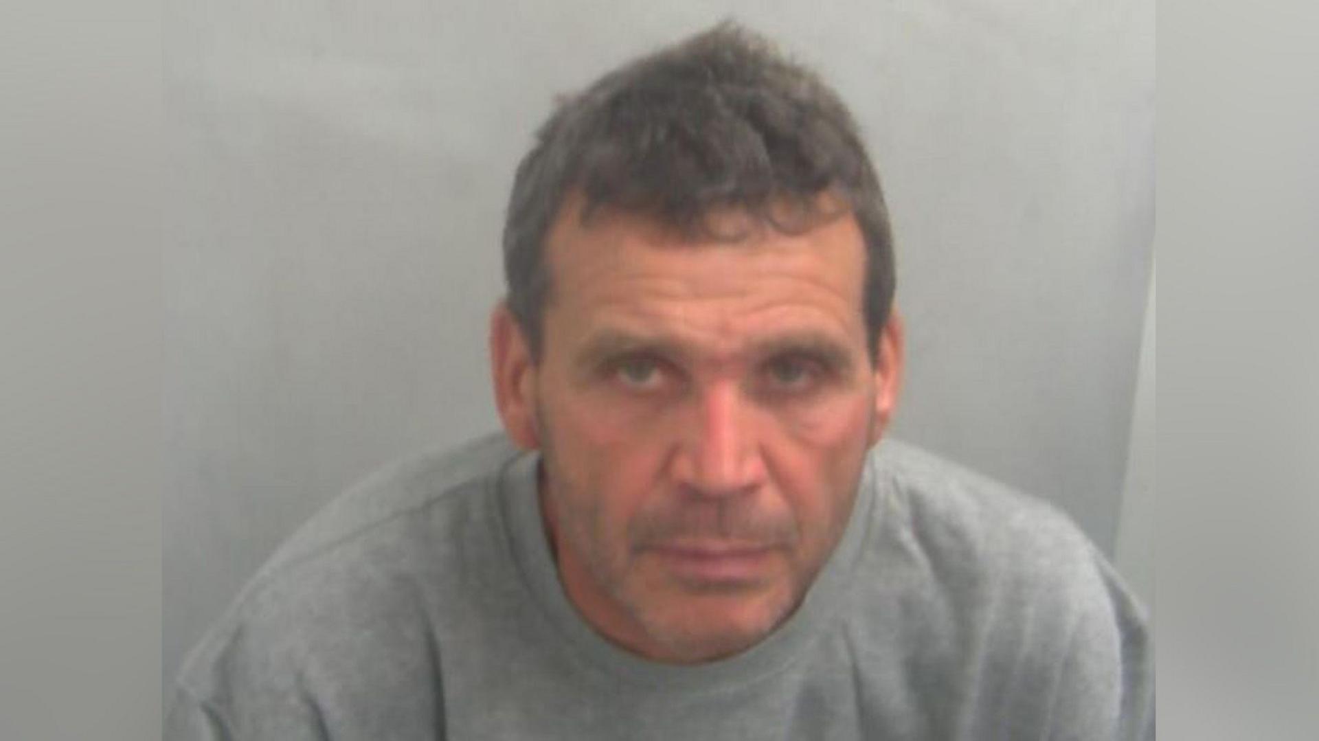 Calogero Ricotta is in custody wearing a grey jumper. He has greying hair and is unshaven.