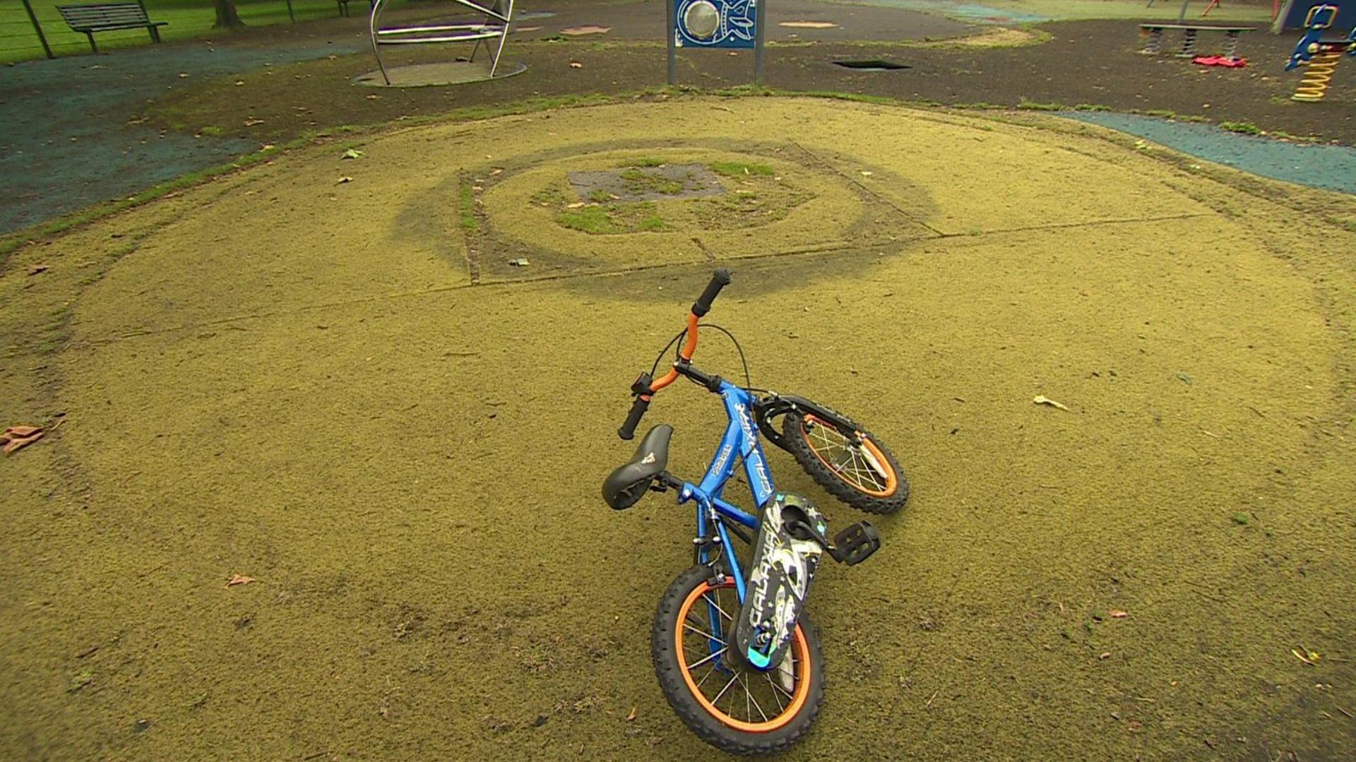 Fake grass in a playground. On the grass, you can see dark outlines from where play equipment used to be. In the foreground, there is a bike.