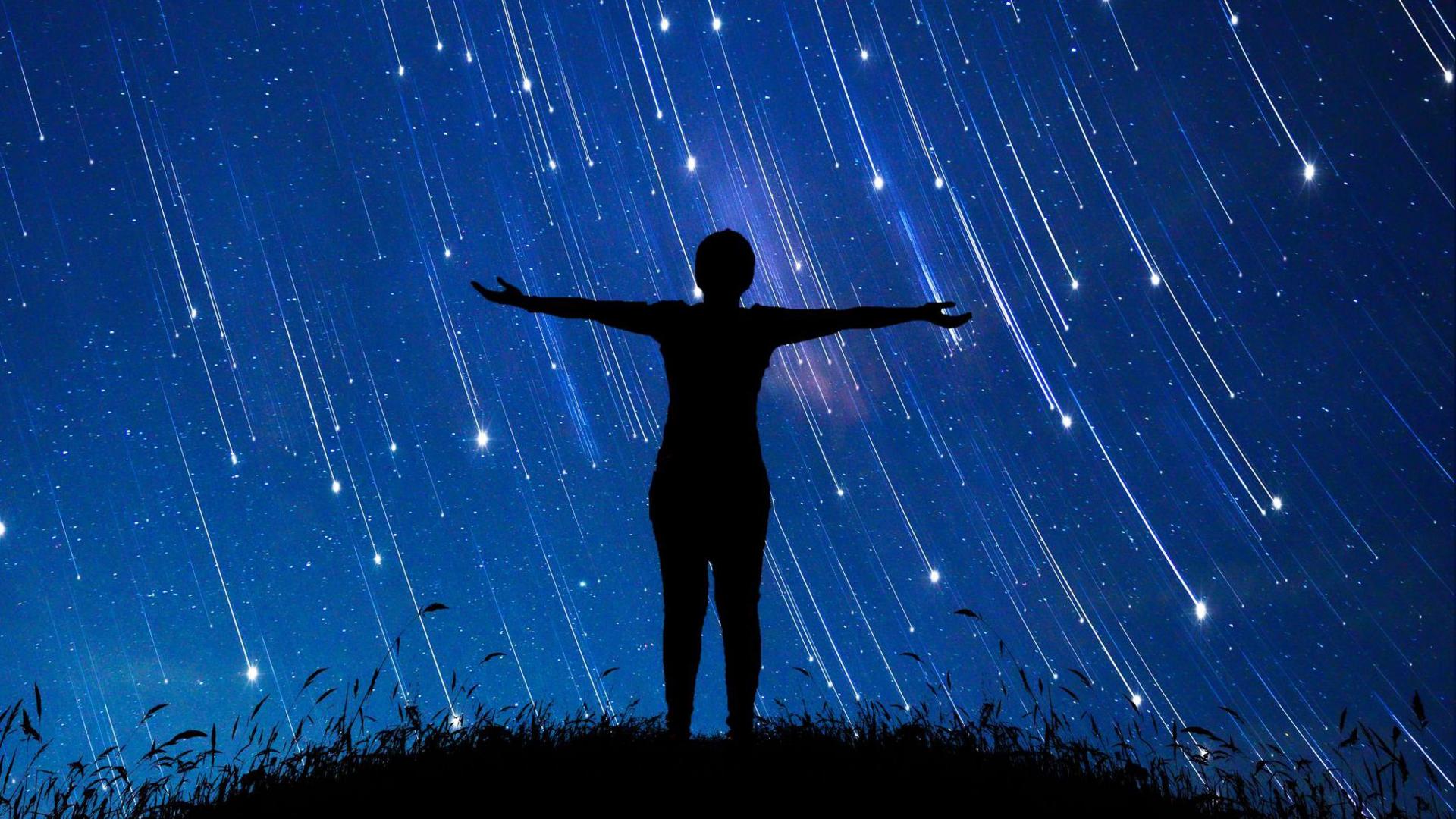 Shadow of a person stood with their arms up with shooting stars in the background