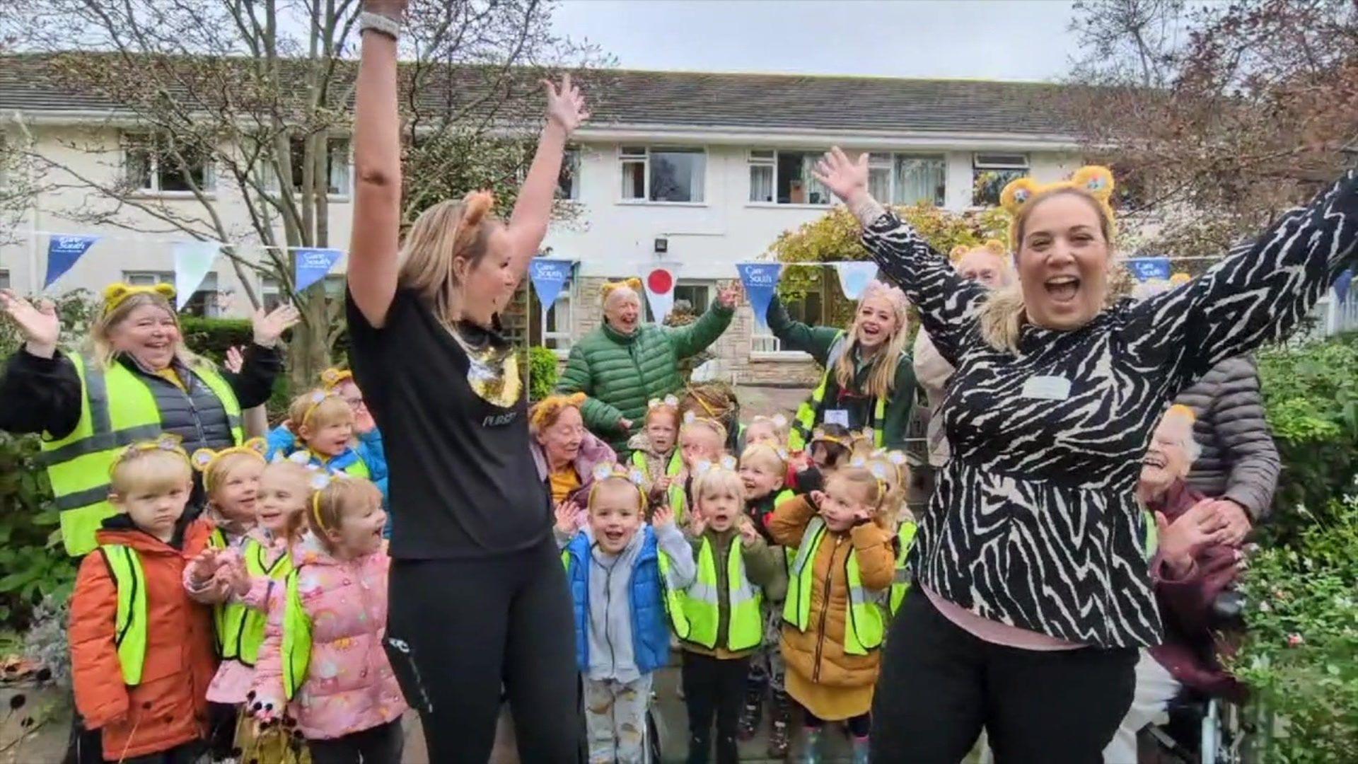 Adults and children stood in a garden with their hands in the air as they cheer