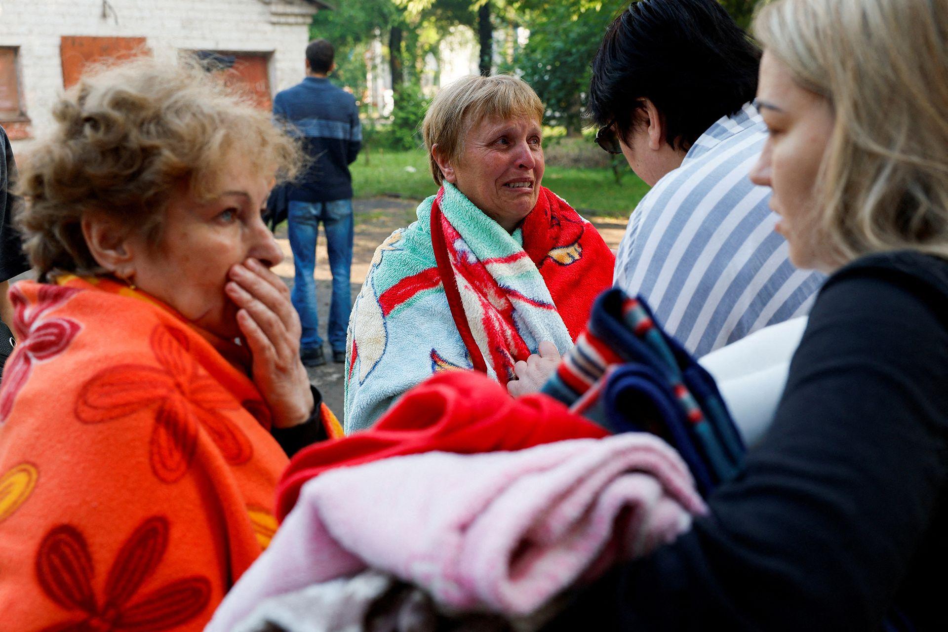 A group of shocked, concerned-looking residents gather outside with blankets around them and consoling each other after a strike on a residential building in Kryvyi Rih, central Ukraine in June 2023. 